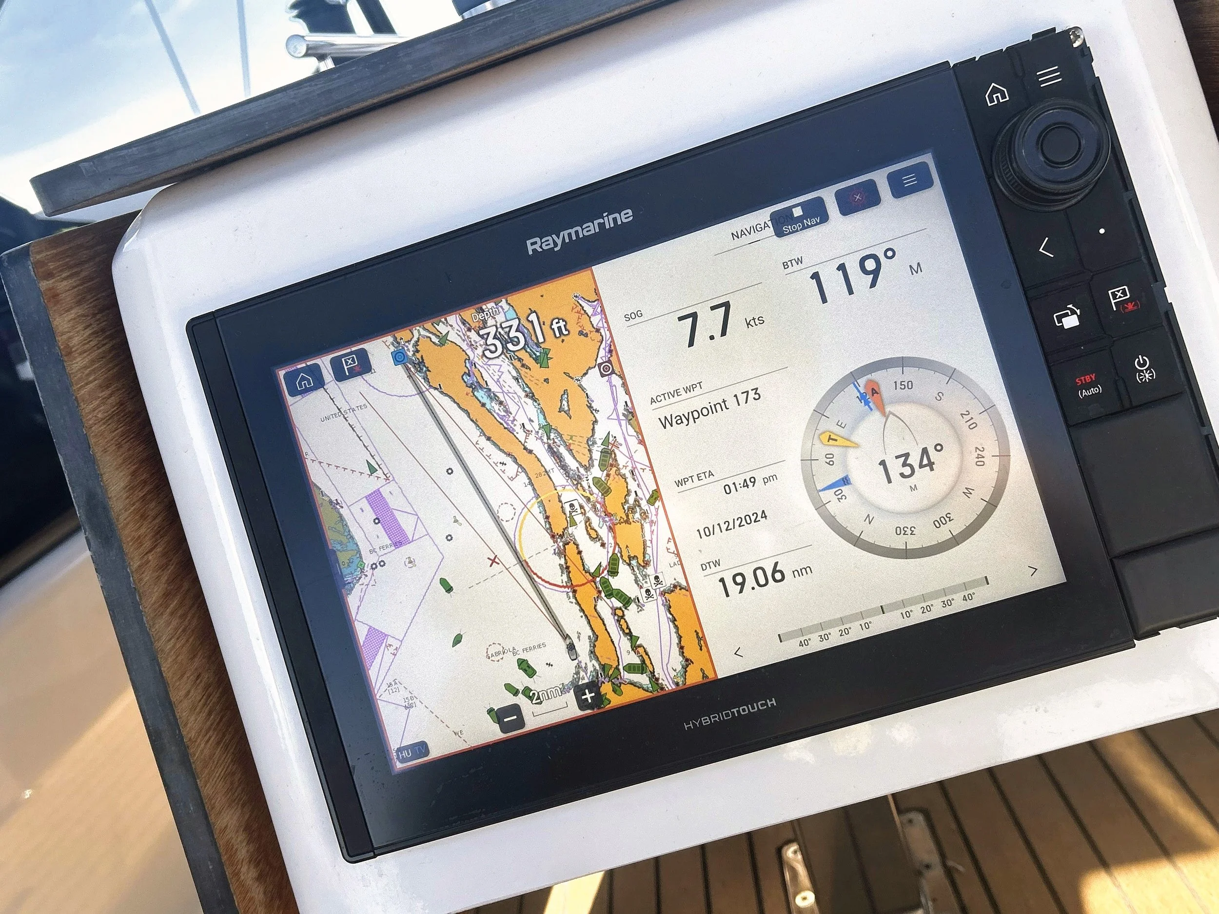A digital navigation display on a boat showing a detailed map of the surrounding waters and land, with navigation information including speed, distance, course, and heading.