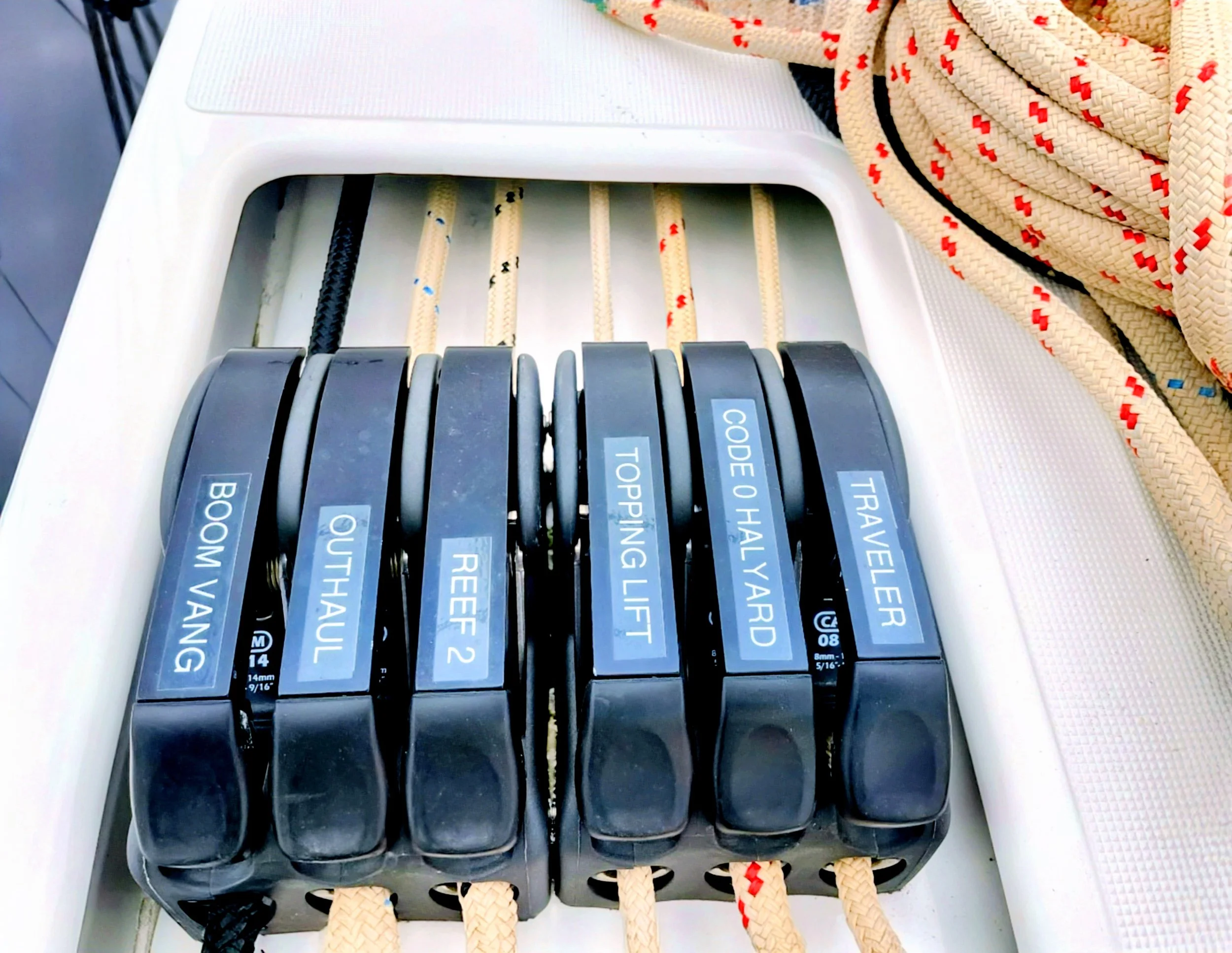Close-up of a set of nautical navigation tools with labels, placed on a white surface with a rope and netting nearby.