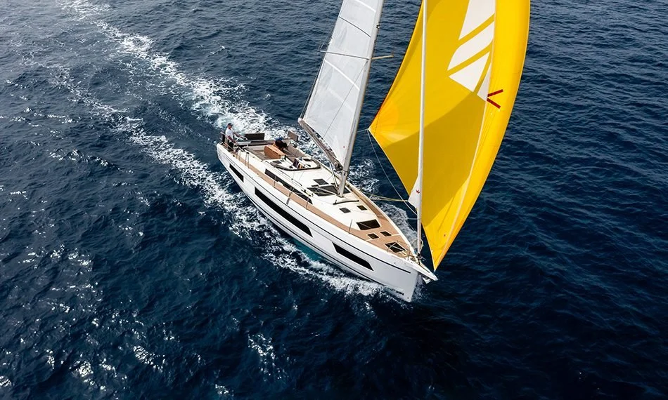 An aerial view of a sailboat with yellow and white sails sailing on the open ocean.