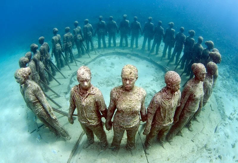 Underwater sculpture of a circle of seated and standing human figures holding hands.