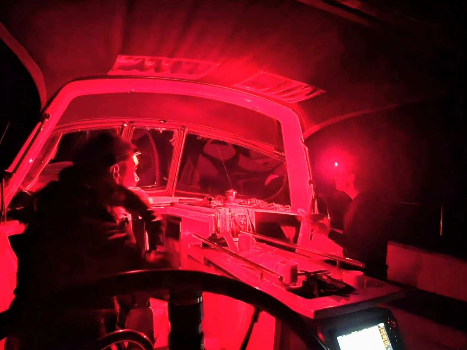 A person in a wheelchair working on a boat while illuminated by red light at night.