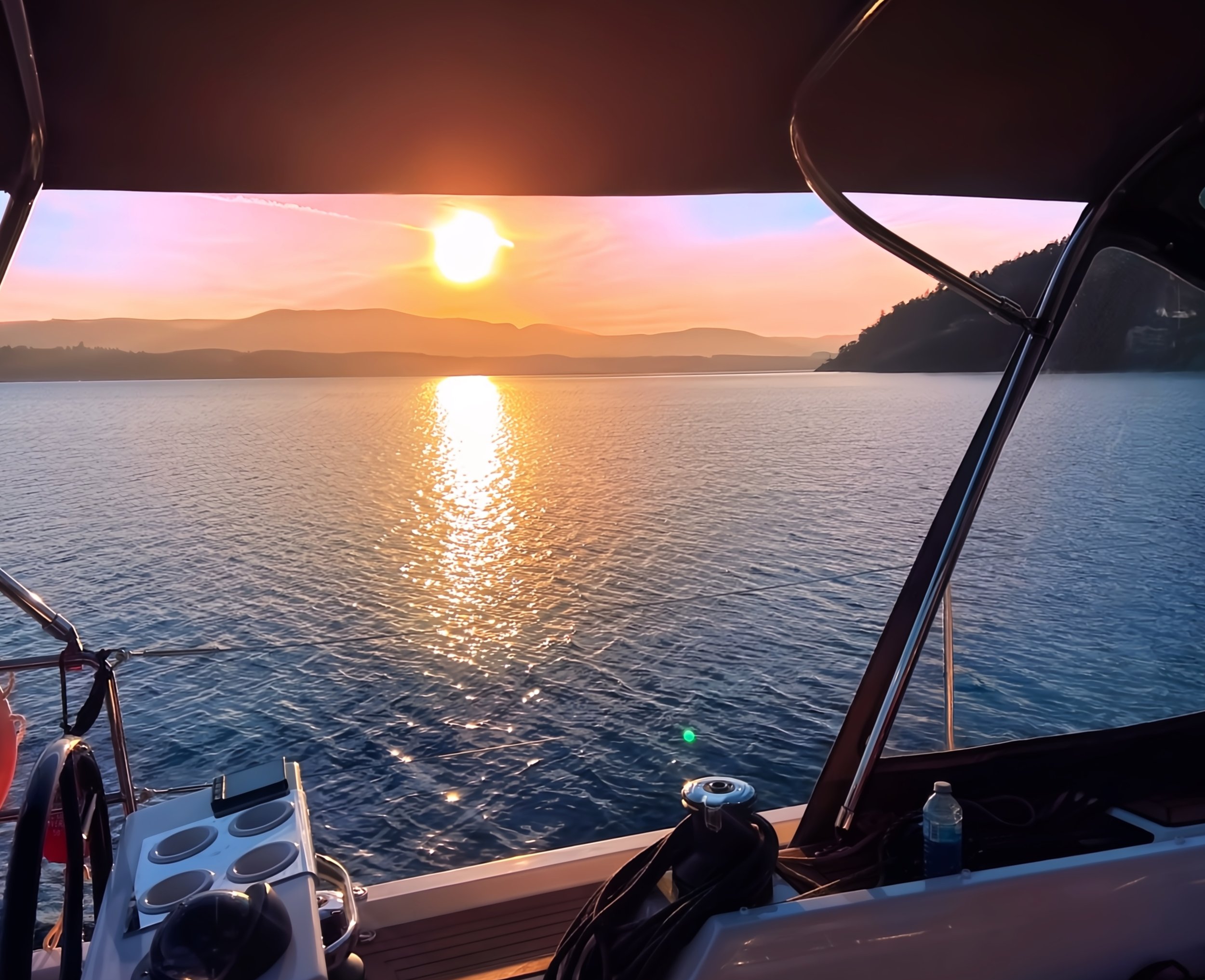 View from a boat overlooking a lake at sunset with mountains in the distance.