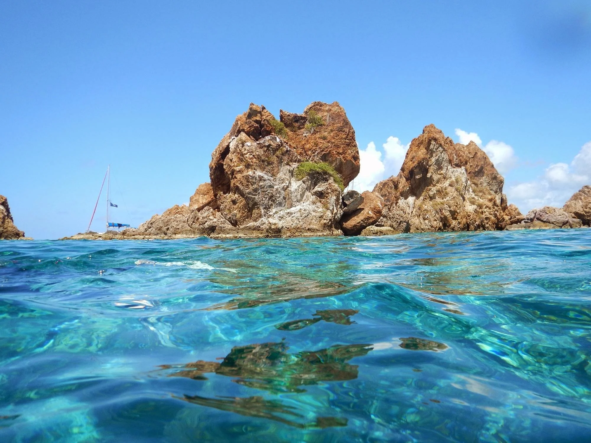 Clear blue water with rocky islands and a sailboat in the distance under a partly cloudy sky.