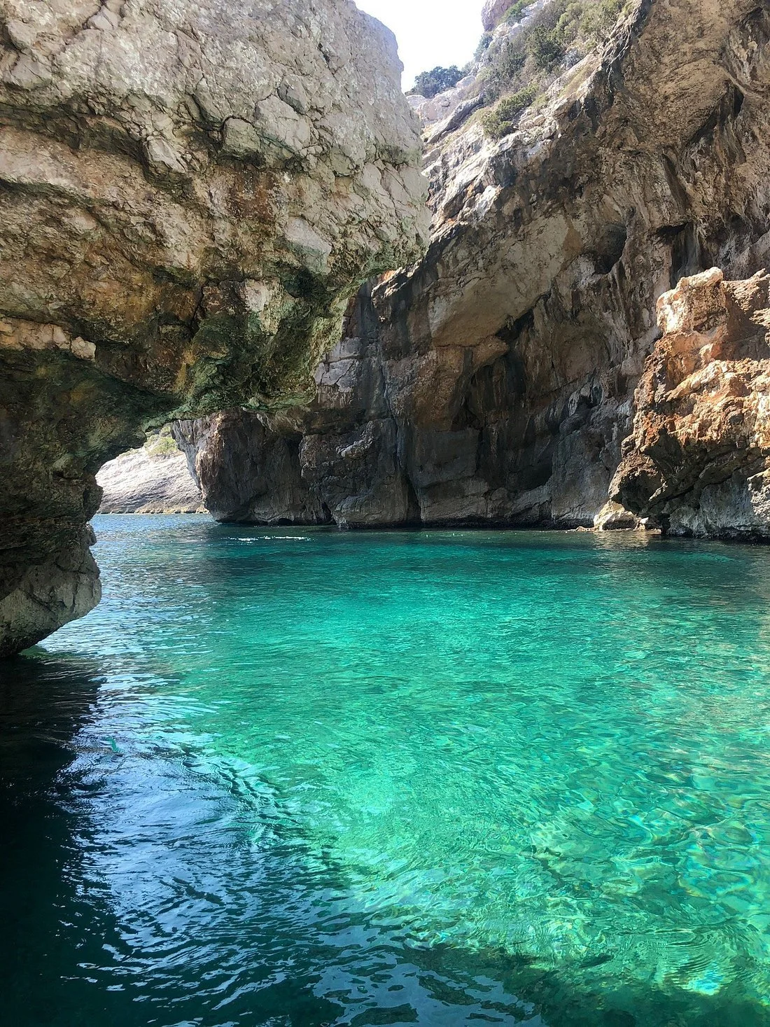 Crystal clear turquoise water between large rocky cliffs with a small waterfall in the background.