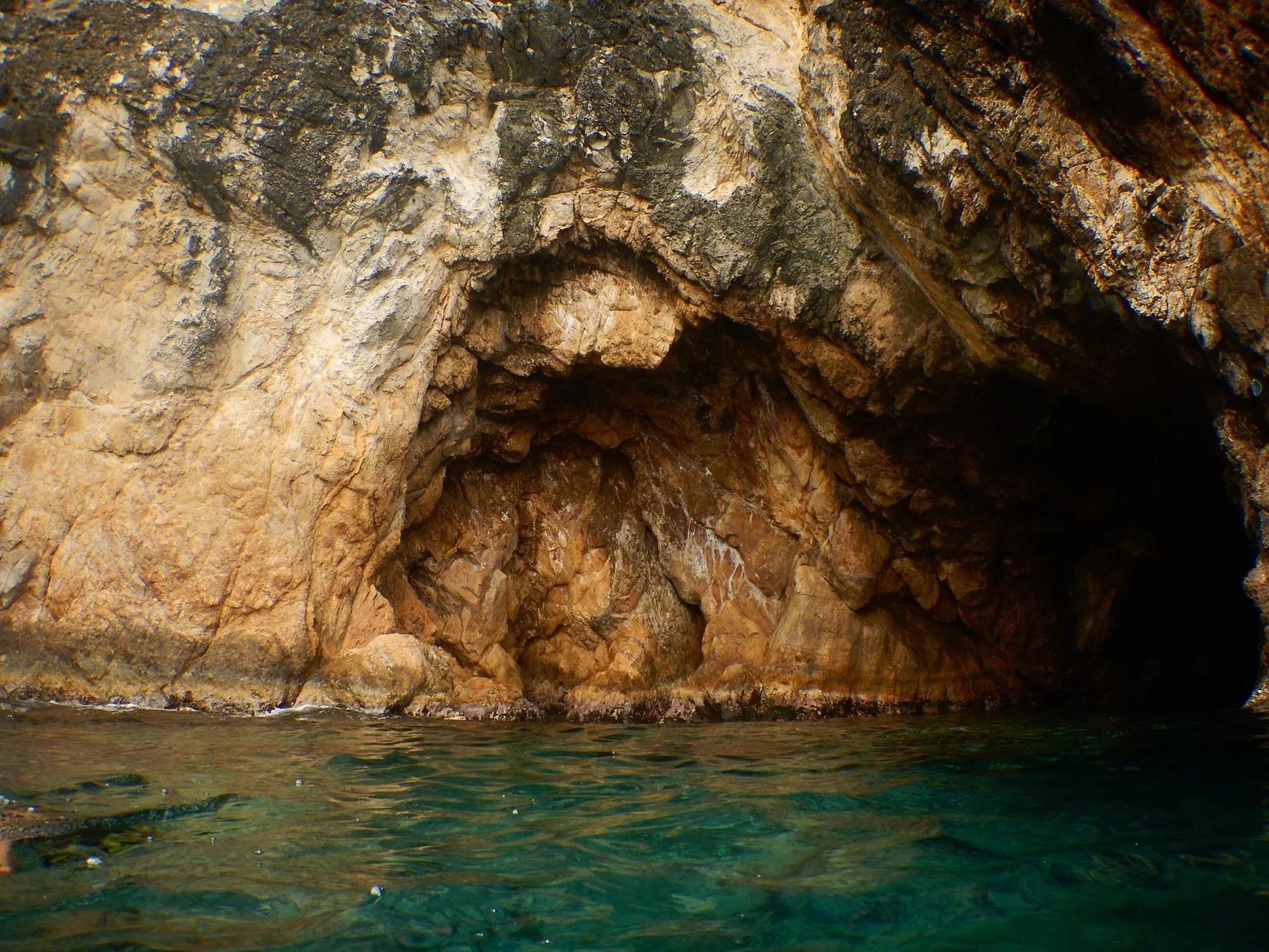A rock cave partially submerged in water with brown and black textured rocks.