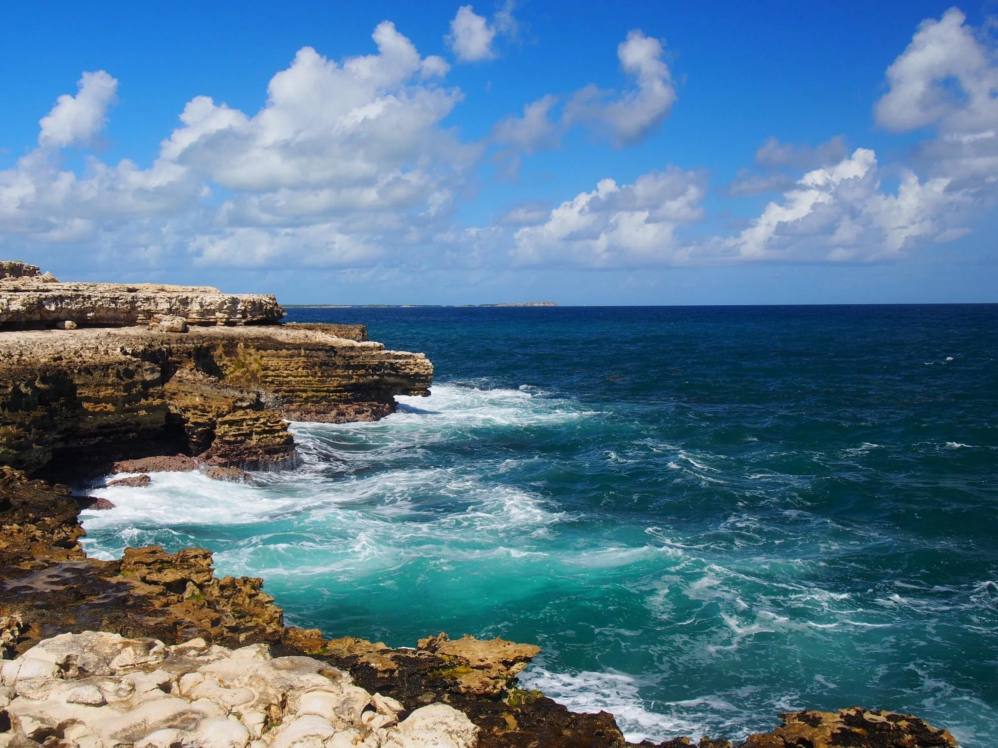 Cliffs overlooking the ocean with clear blue skies and white clouds.