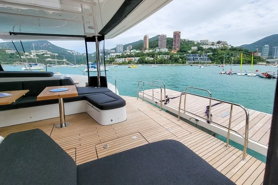 View from the deck of a yacht showcasing a marina with boats, a cityscape with high-rise buildings, green hills, and boats on the water.