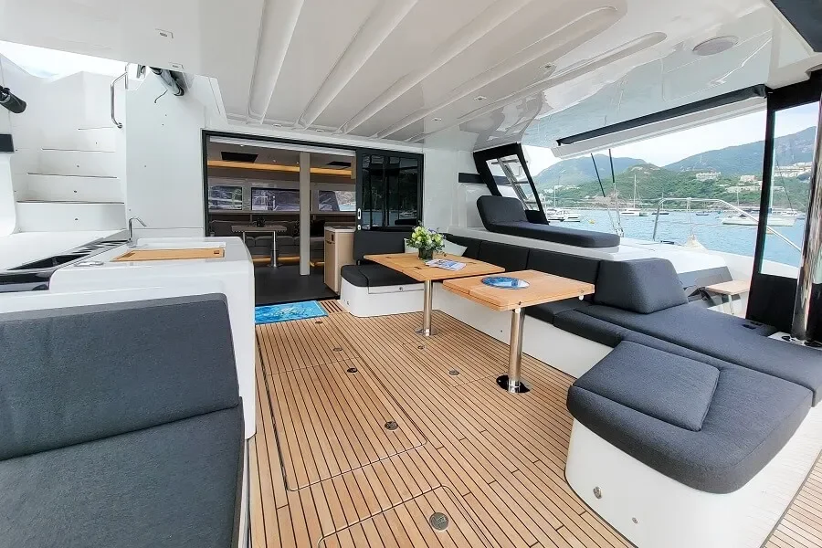 Interior of a yacht with seating area, wooden tables, a view of the water and hills outside through large windows