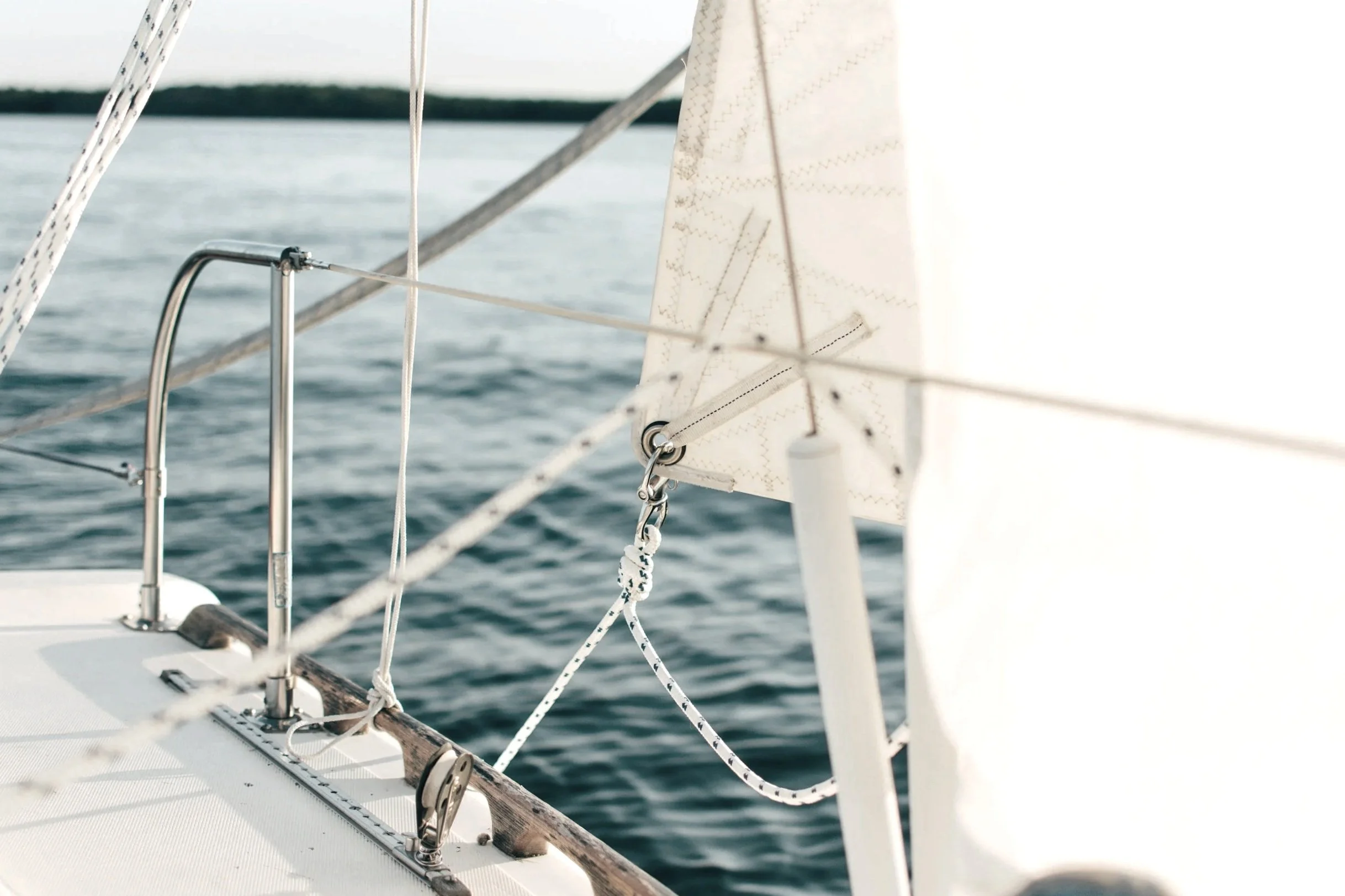 Close-up of a sailboat's rigging and sail with a body of water in the background.