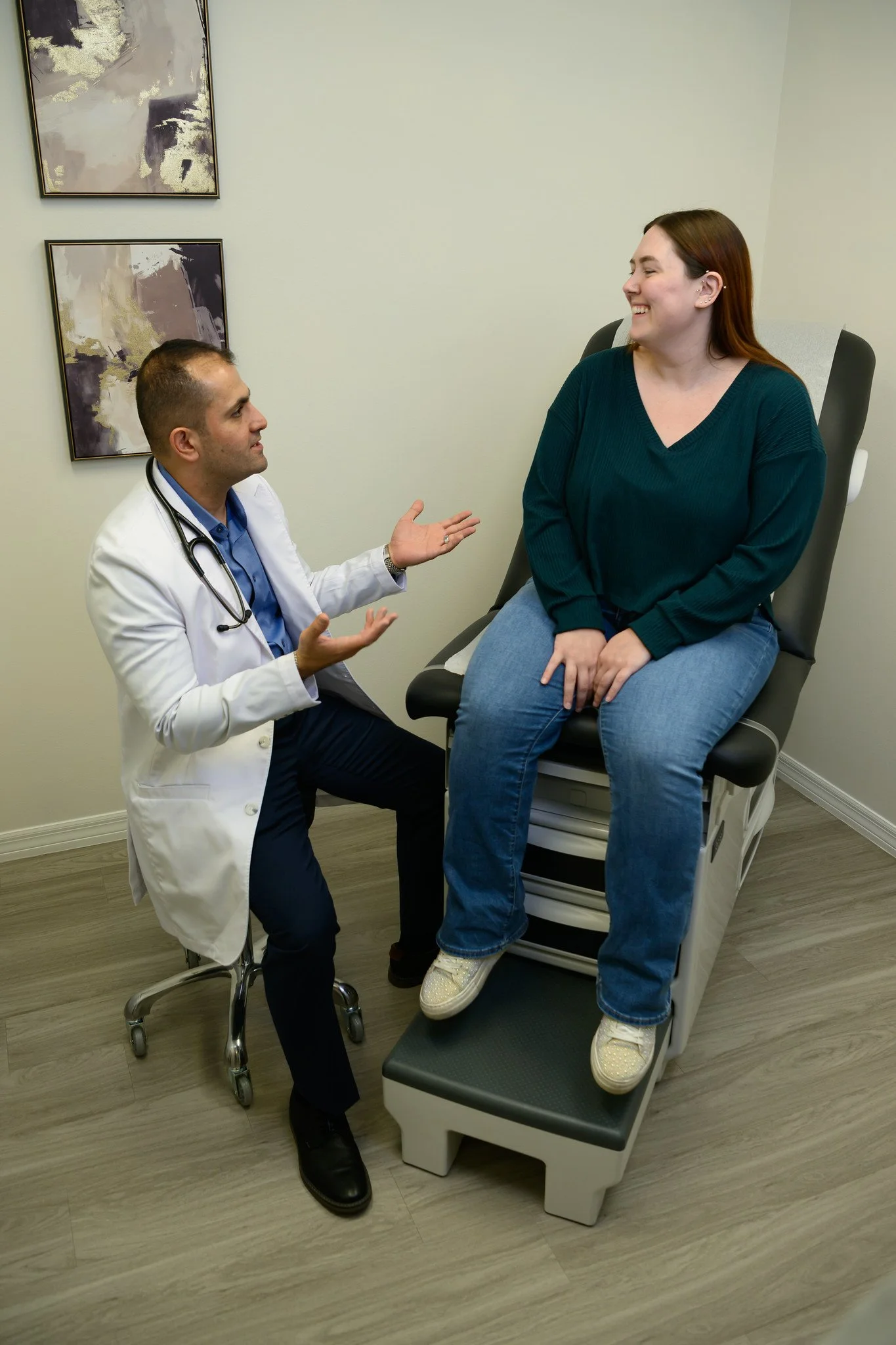 Dr. Said Awad talking to a female patient sitting on an examination chair in a medical office.
