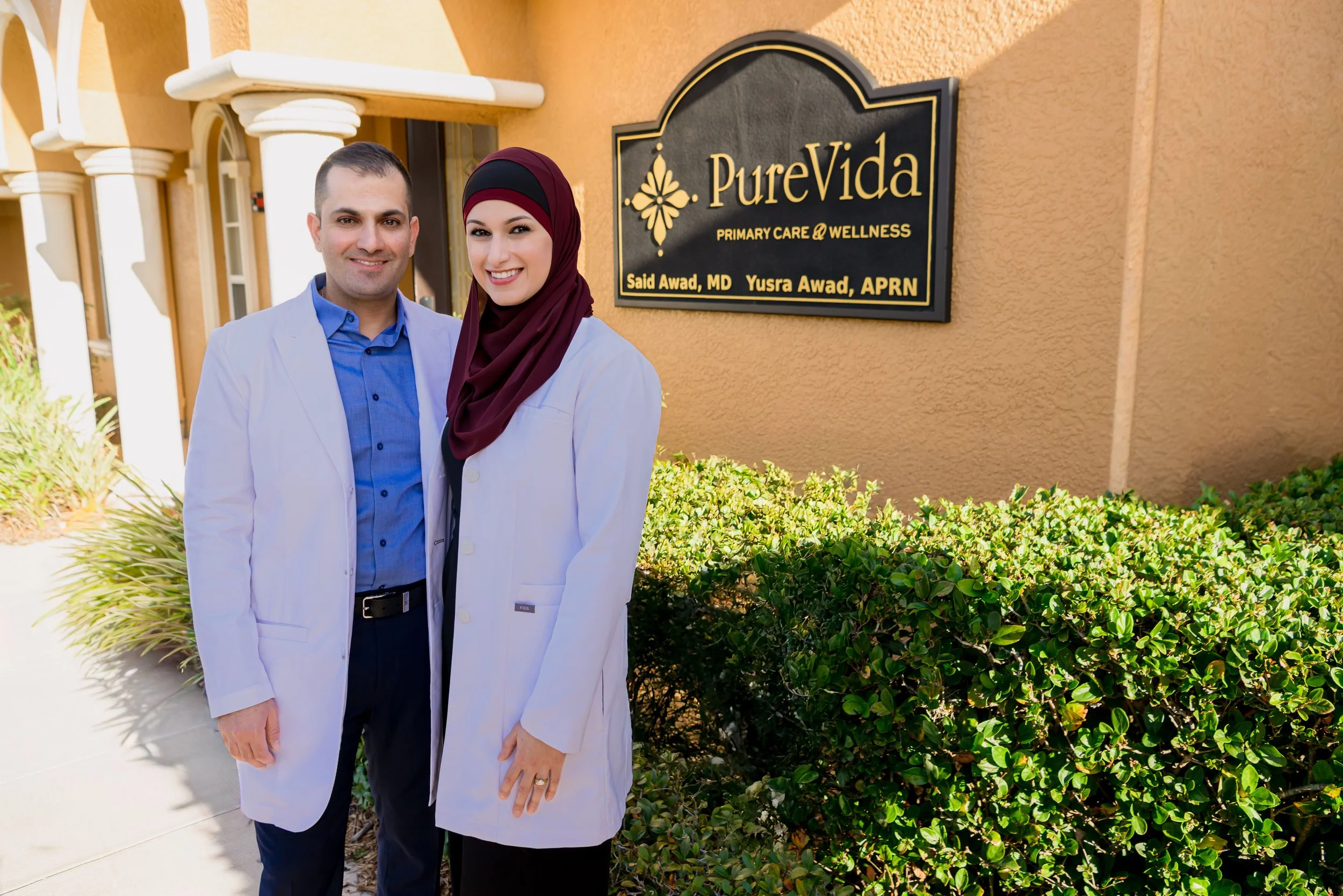 Dr. Said Awad Nurse Practitioner Yusra Awad standing outside their clinic with a sign that reads "Pure Vida Primary Care & Wellness."