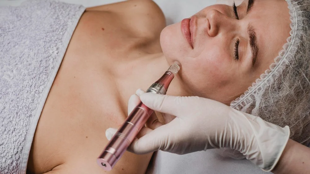 A woman is receiving a cosmetic injection in her chin area in a medical setting, with a technician wearing gloves administering the treatment.