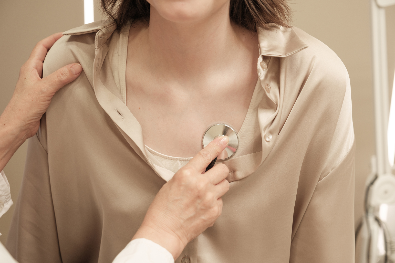 A healthcare professional is using a stethoscope on a woman's chest during a medical examination.