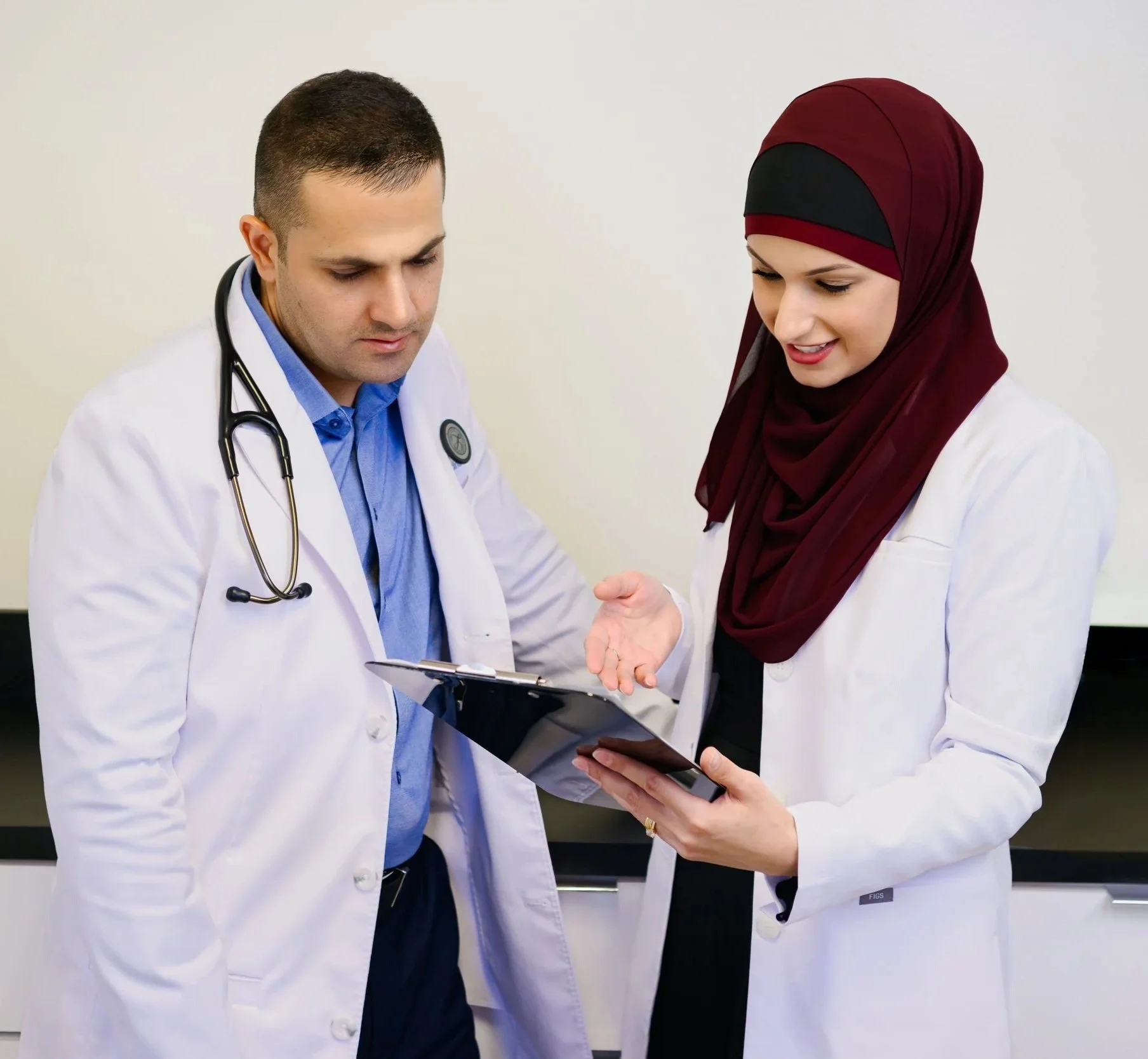 Dr. Said Awad Nurse Practitioner Yusra Awad wearing white lab coats, reviewing a medical chart or tablet together in a clinical setting.