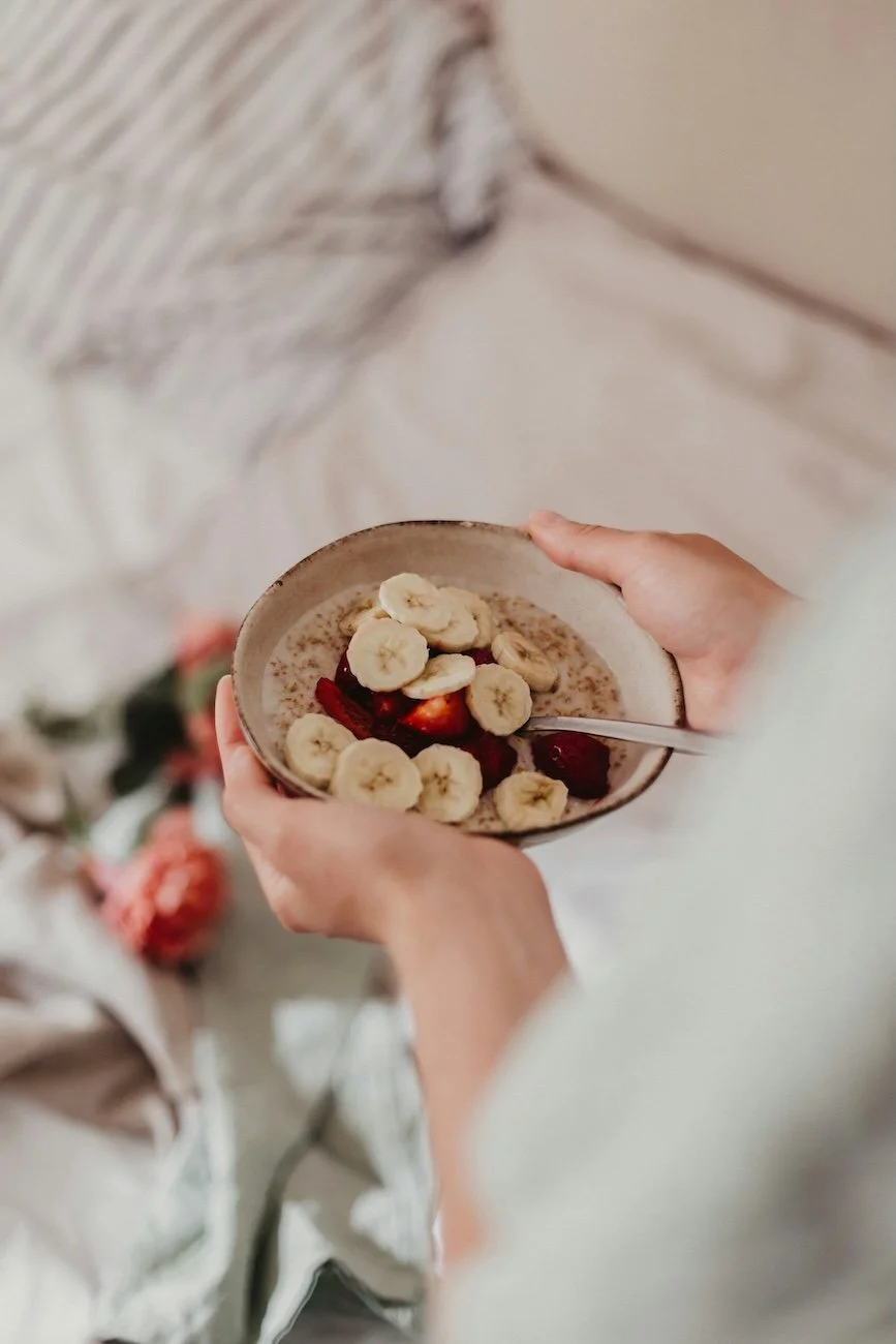 Client-focused naturopathic care with advanced health assessments Person holding a bowl of oatmeal topped with banana slices and strawberries, with a spoon inside.