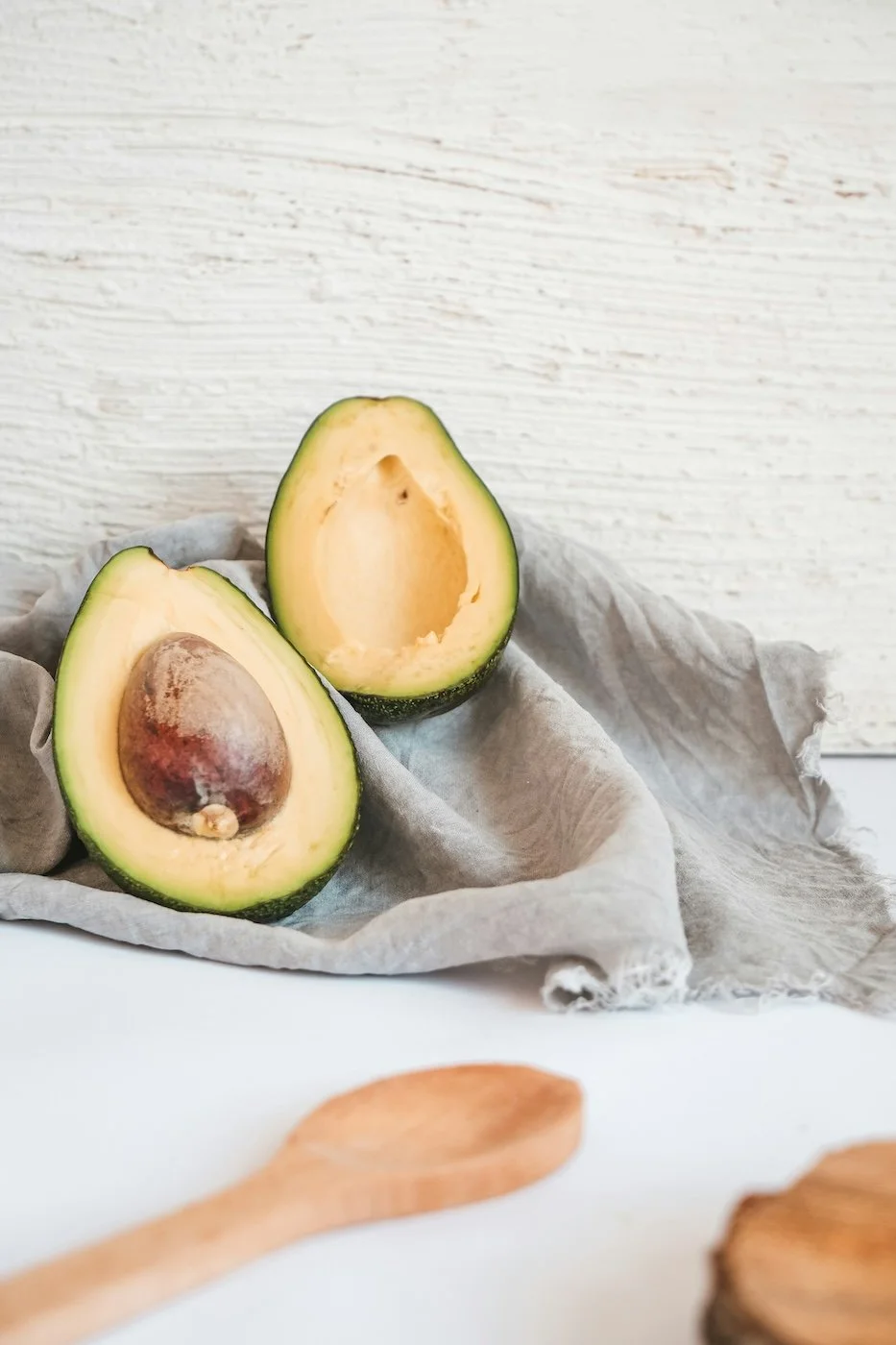 Behind the scenes of product development and supplement formulation Half an avocado with pit and half without, resting on crumpled gray cloth against a light wooden wall.