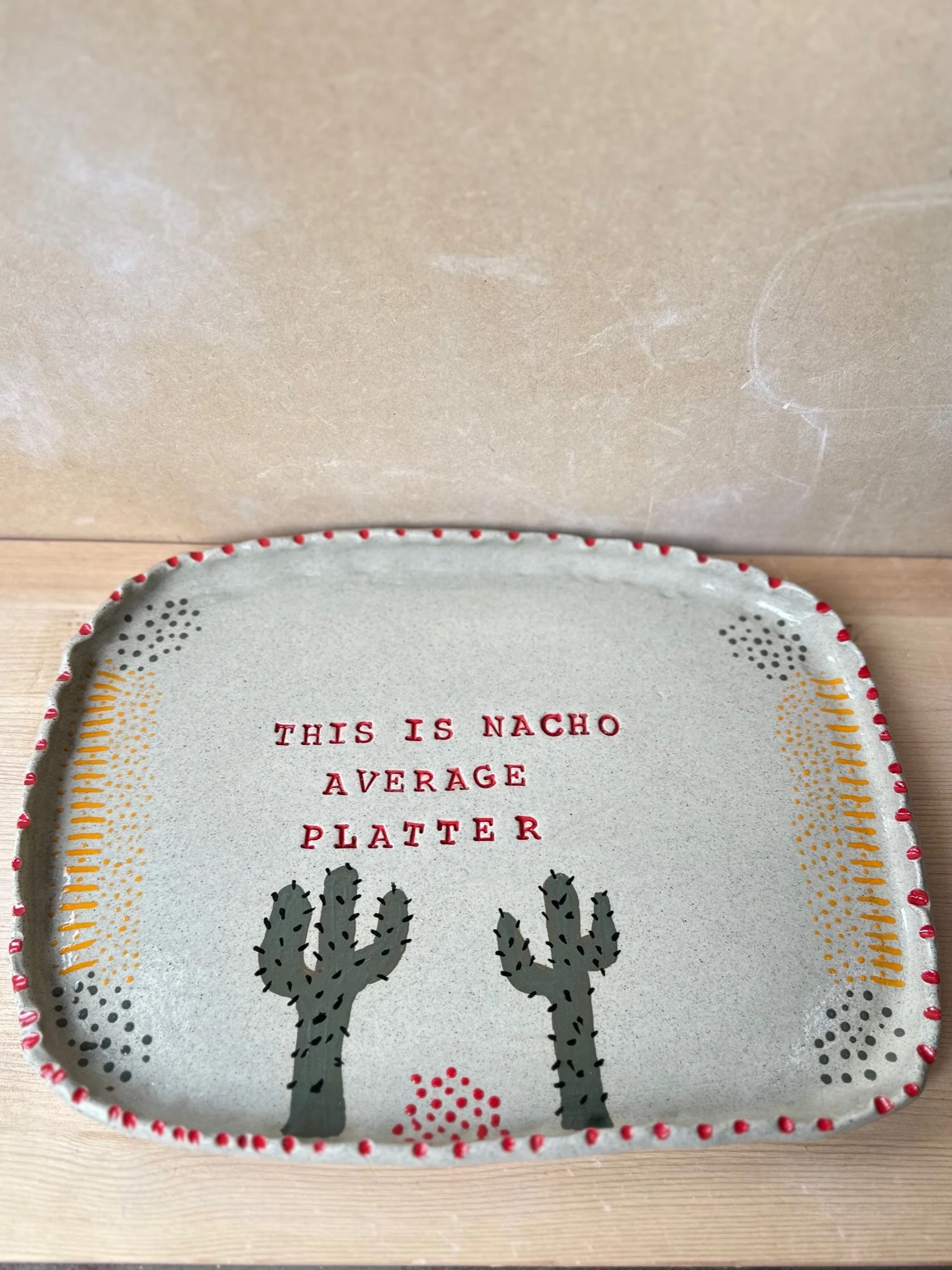 A large platter with red dots on the outside and yellow and green inside.On the inside are two cacti and the saving 'This is nacho average platter'