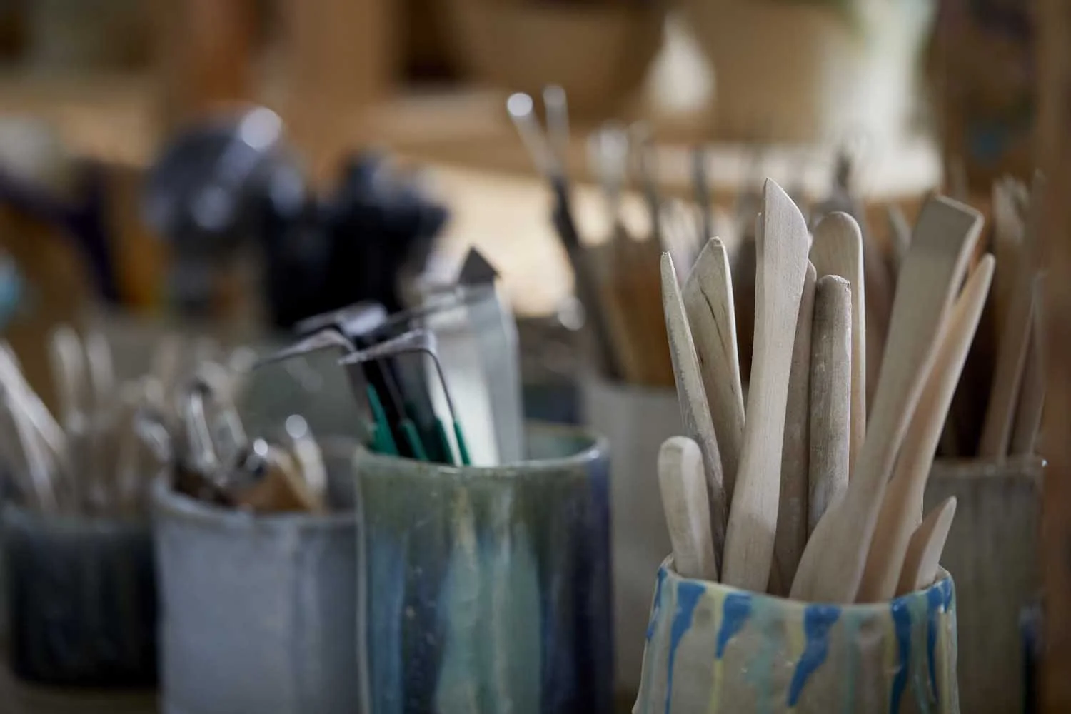 Wooden pottery tools sitting in a coloured pot with metal pottery tools in a blue green pot in the background