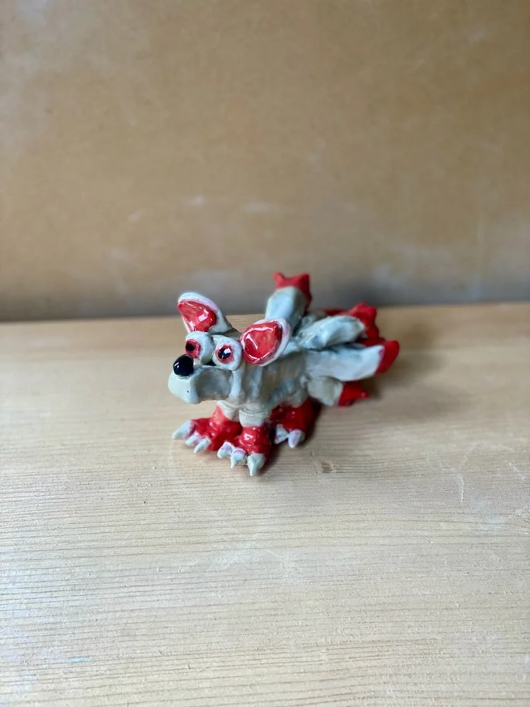 A pale blue and red painted dog sits on a wooden background