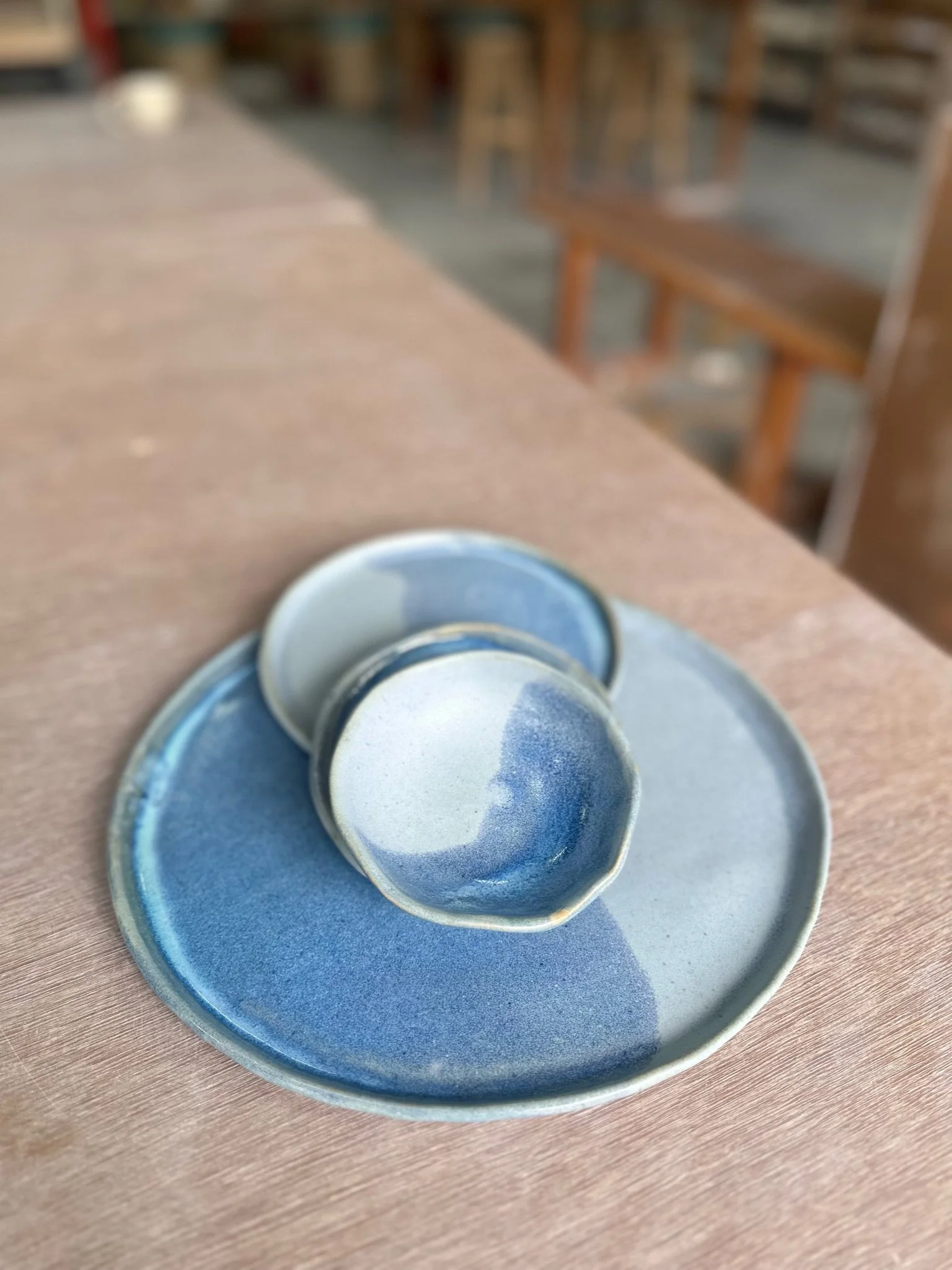 A two tone blue glazed dinner plate sits on a wood background. On top of the plate are a small plate and two small dishes in the same two tone blue.