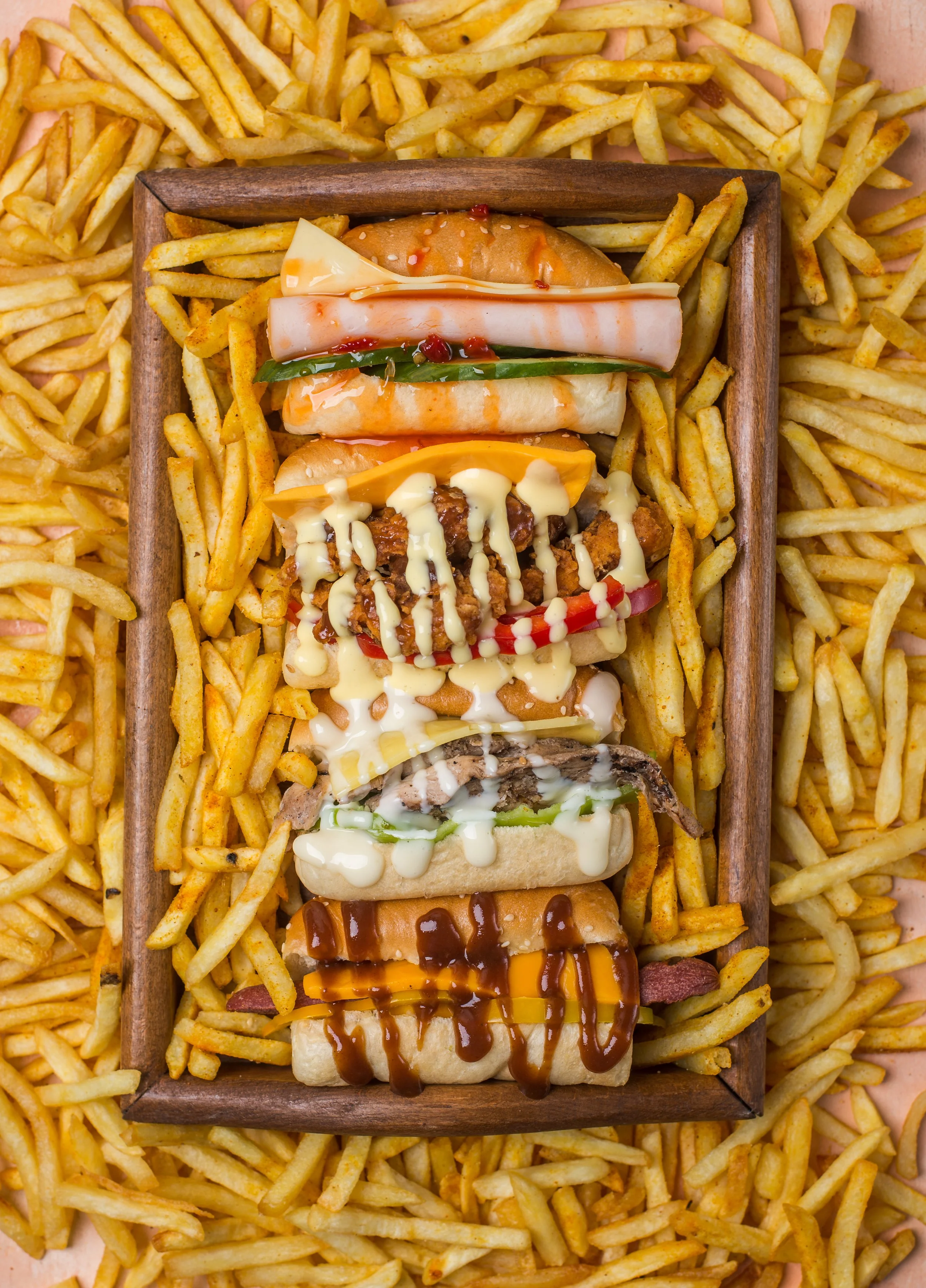 Assortment of mini sandwiches on a wooden tray, surrounded by French fries.