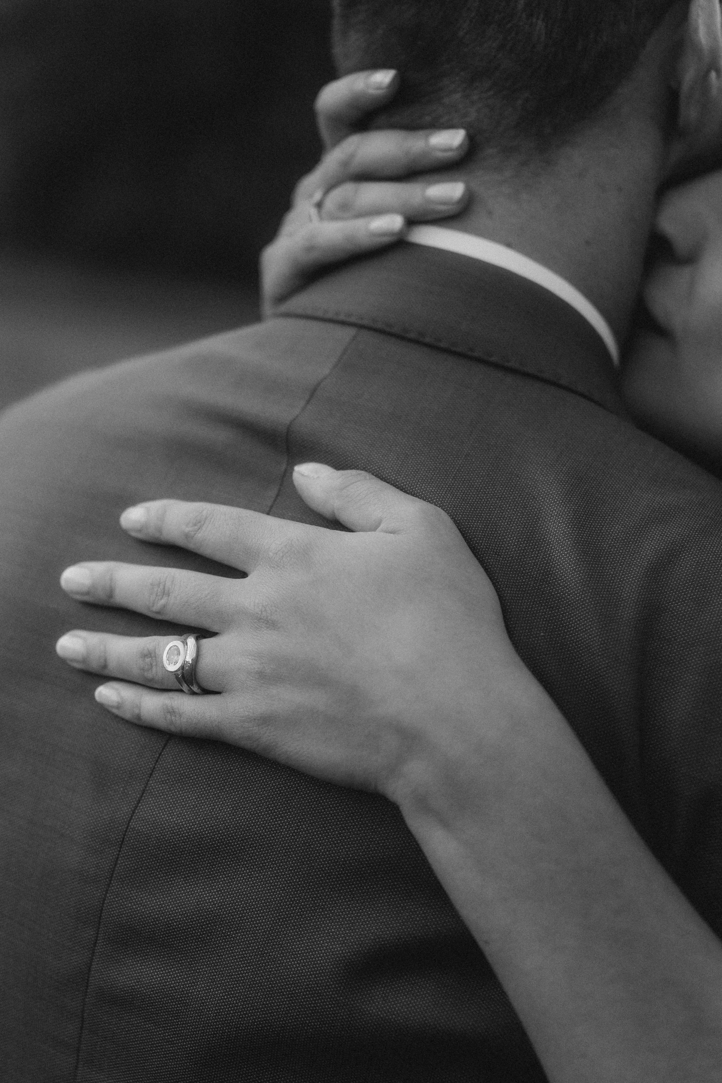 Close-up of a woman’s hand resting on a man’s shoulder, showing a wedding ring on her finger.