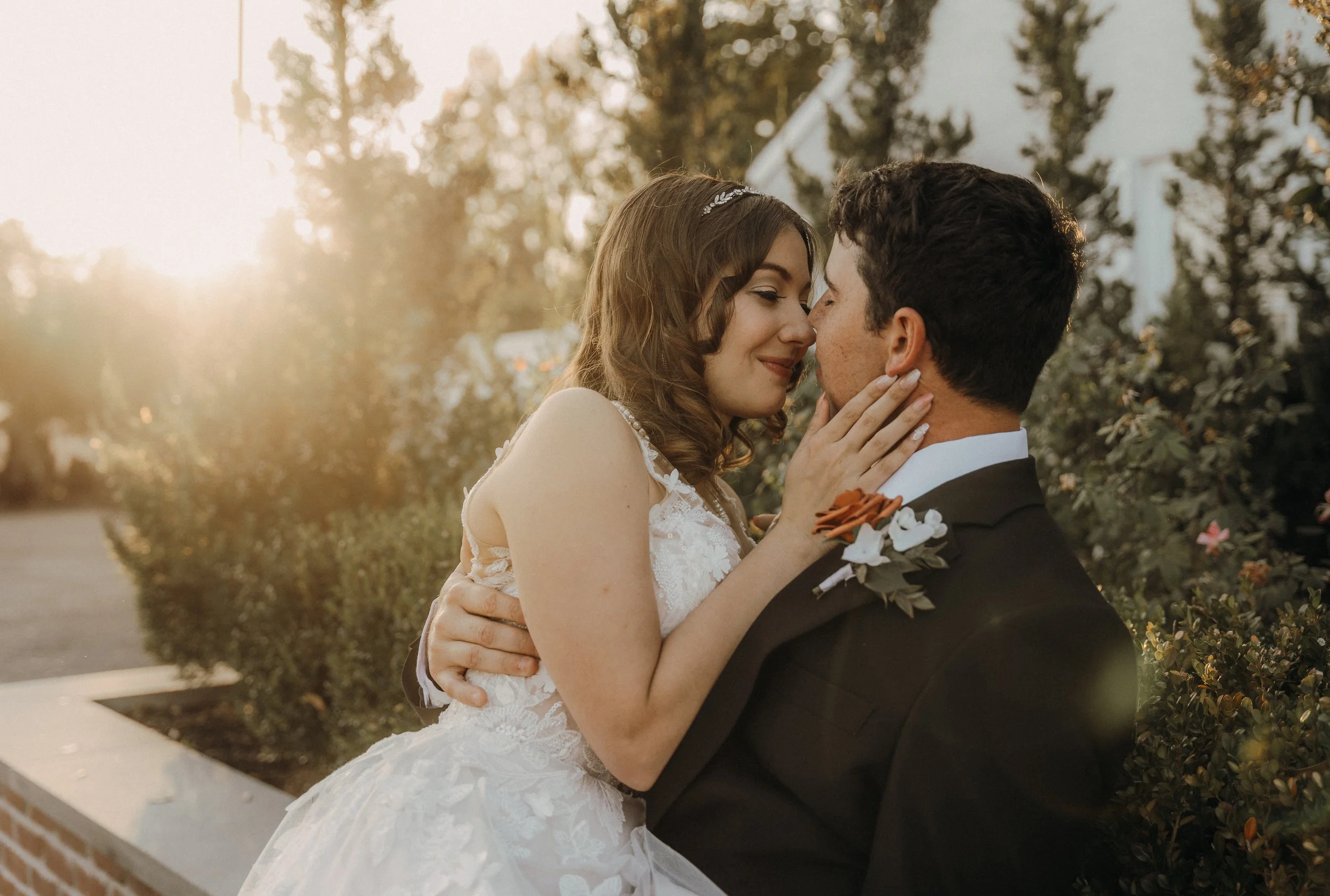 A bride and groom sharing a romantic moment outdoors during sunset, with the bride gently touching the groom's face.