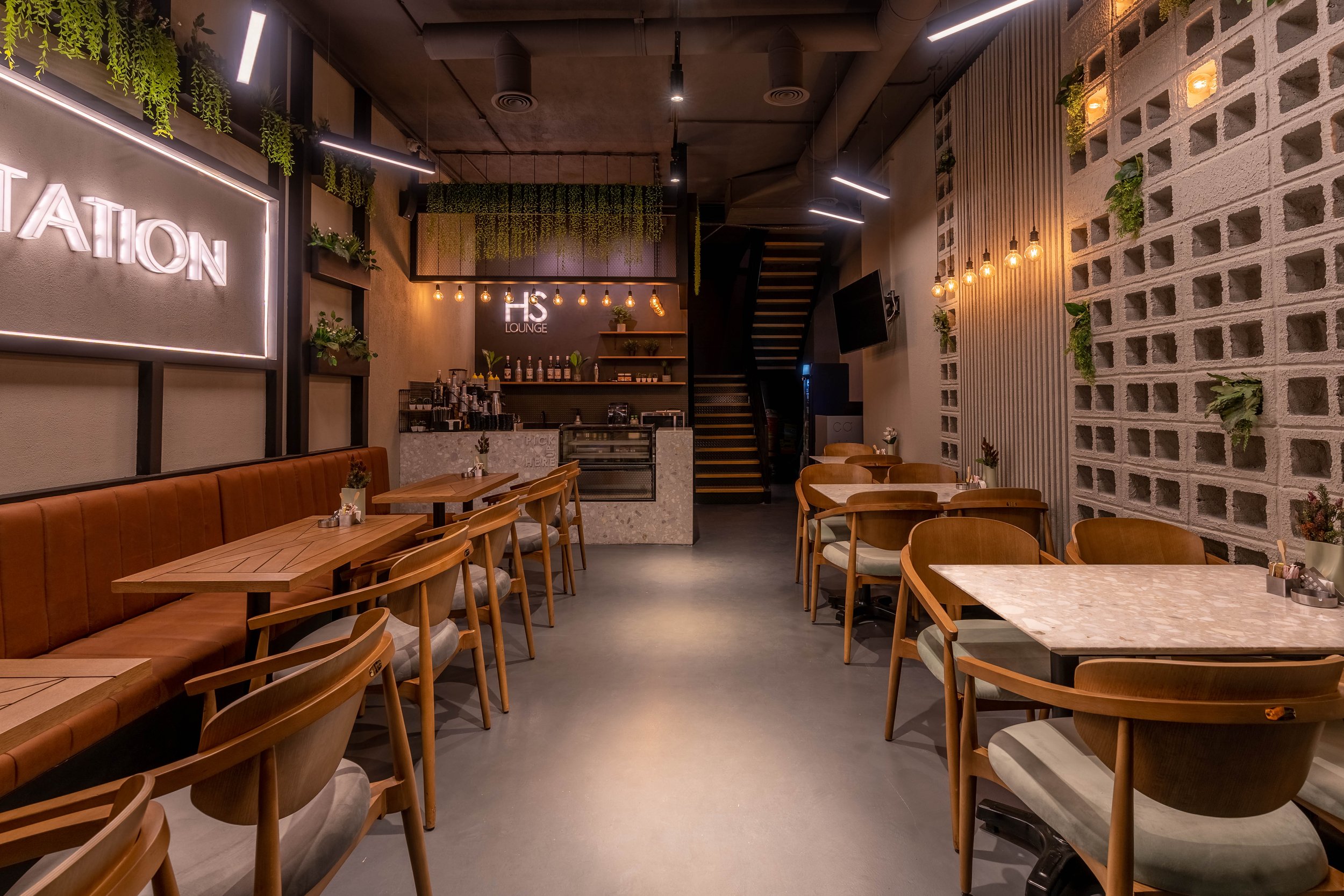 Interior of a modern, cozy cafe with wooden tables and chairs, a brick wall with small plants, and warm lighting.