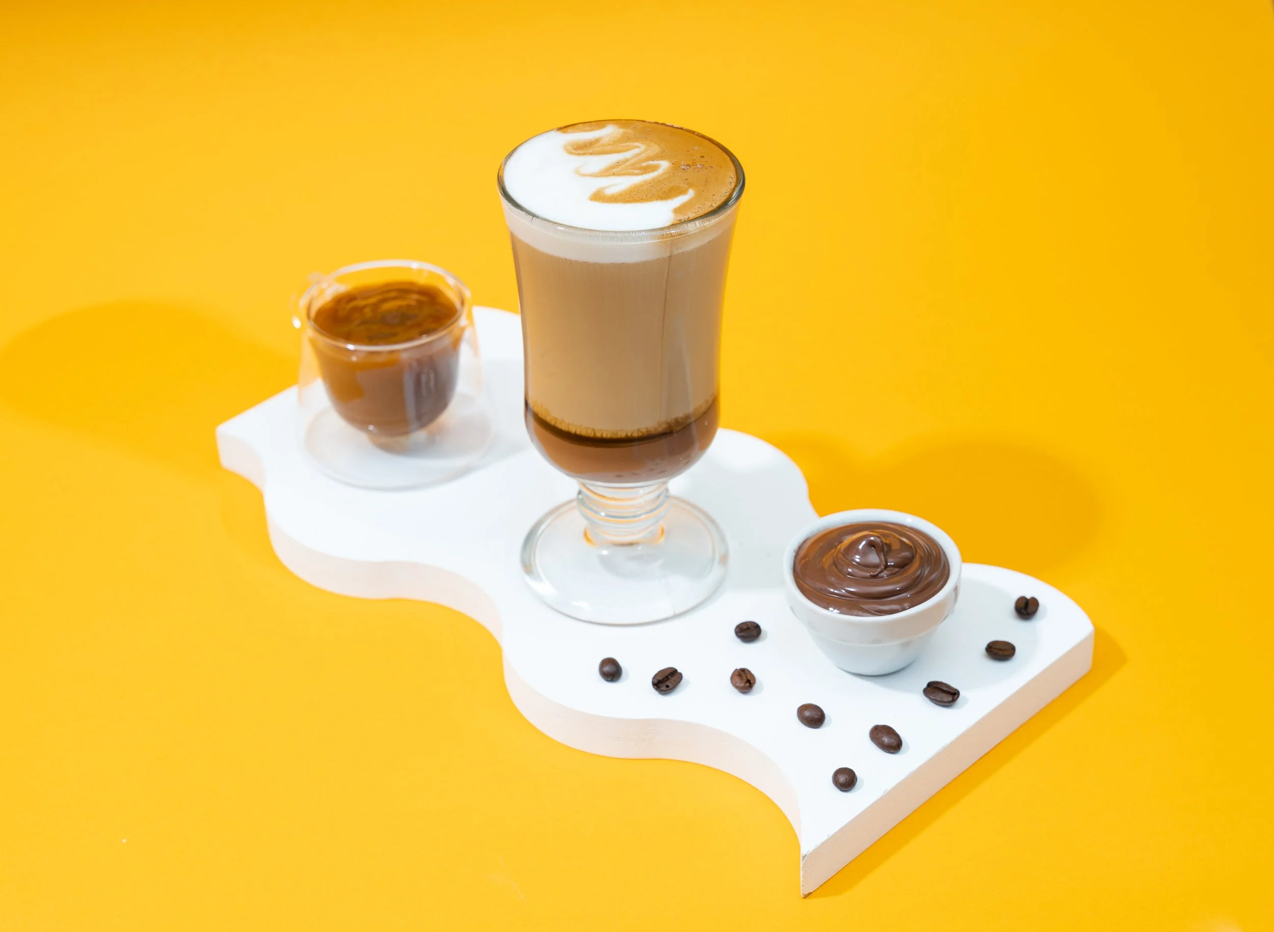 Various coffee drinks and chocolate with coffee beans on a white decorative board against a yellow background.