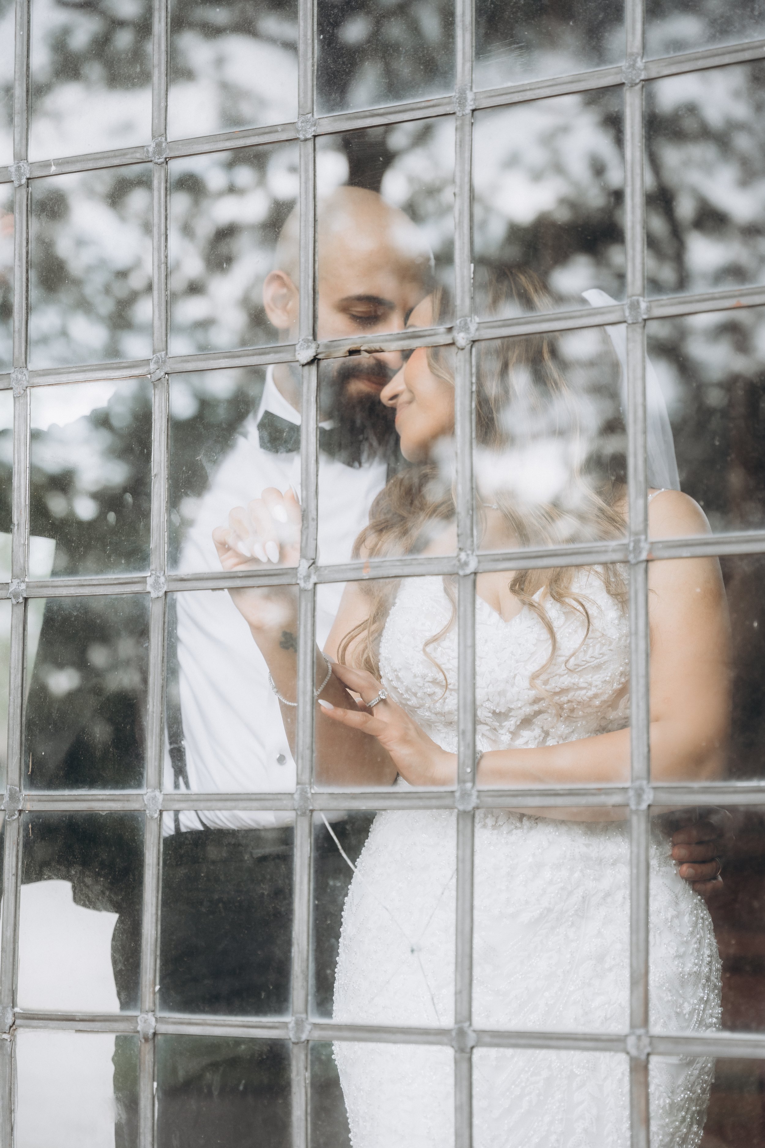 A bride and groom share an intimate moment through a glass window on their wedding day, with snow outside.
