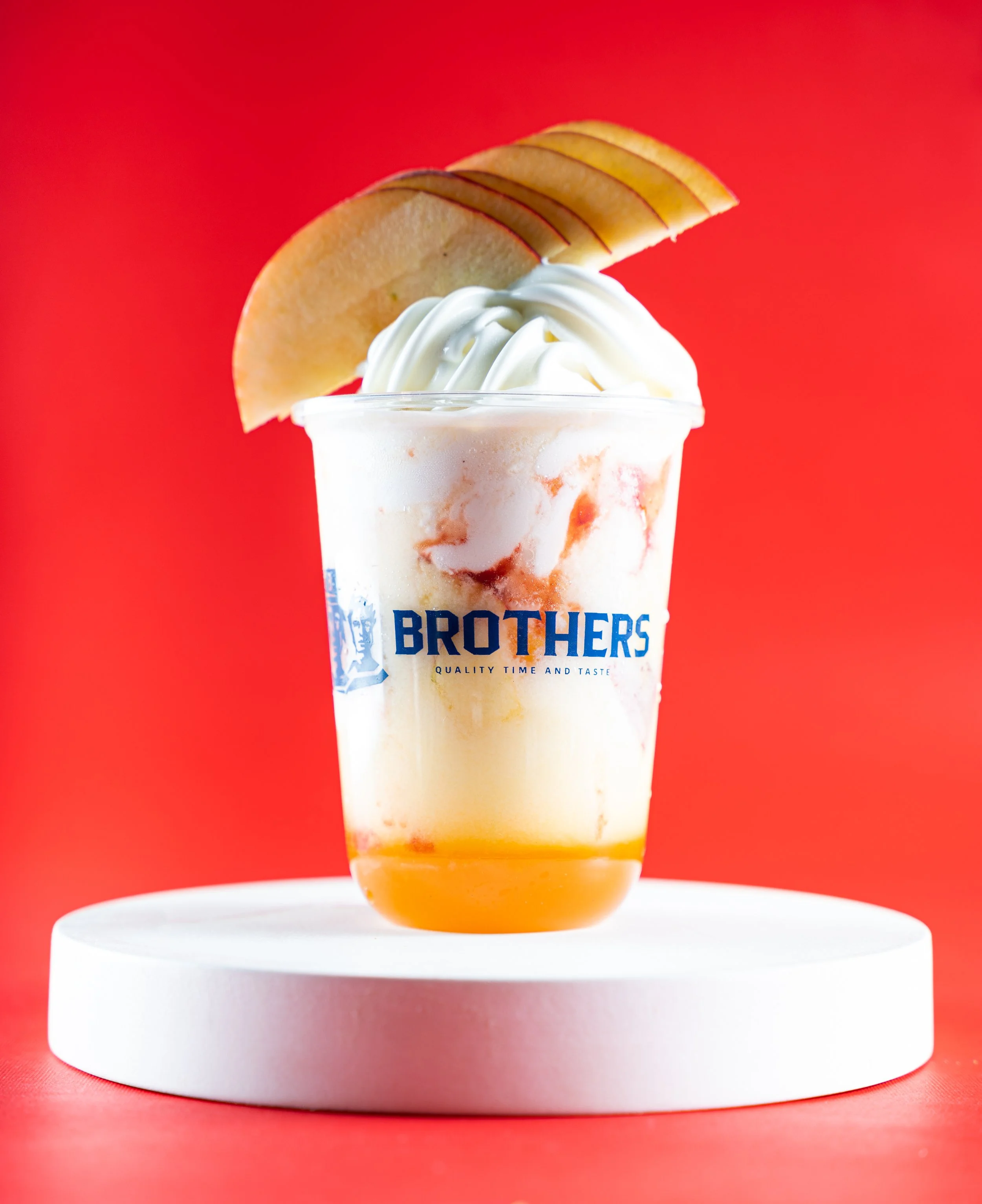 A cup of ice cream with whipped cream, apple slices on top, and a red background.