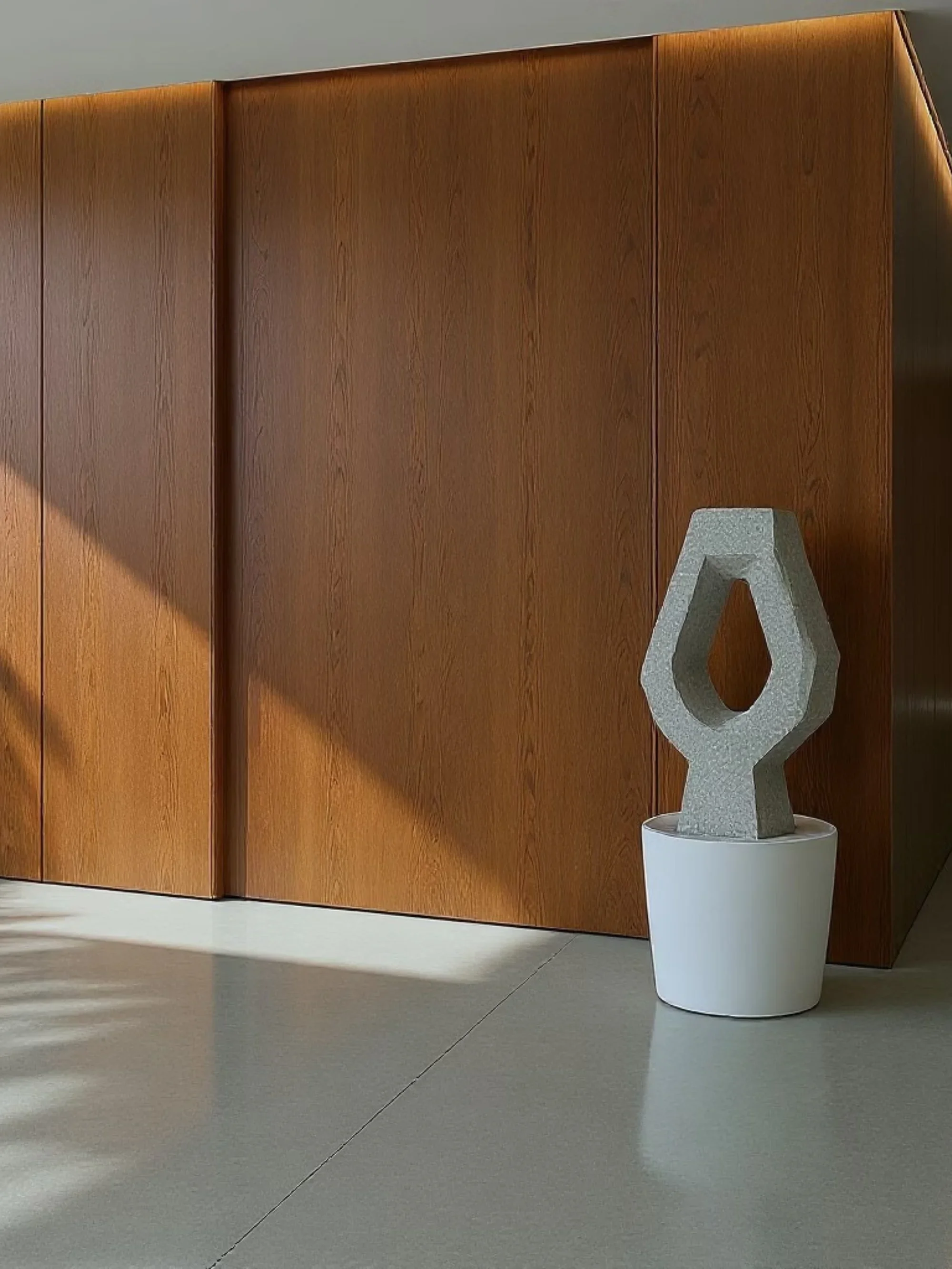 A modern interior with a wooden wall and an abstract sculpture in a white planter.