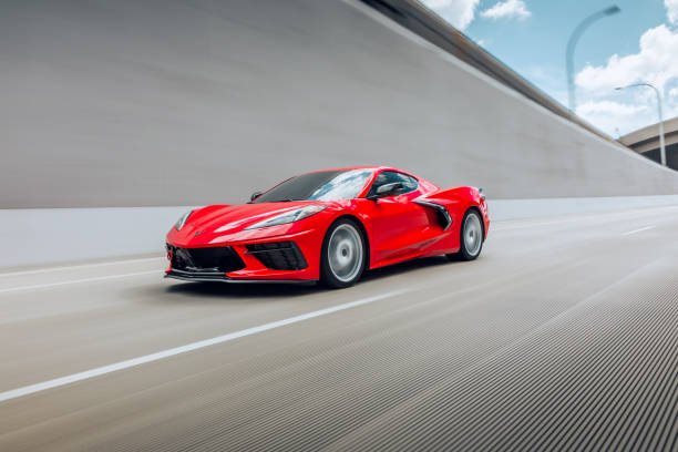 A red sports car driving on a highway with a concrete barrier on the side and a clear sky overhead.