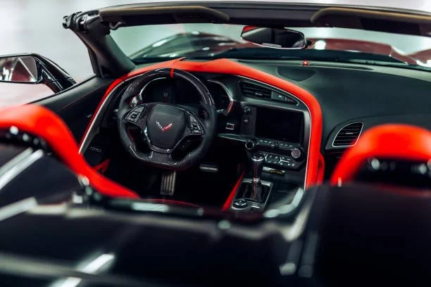 Interior of a convertible sports car with a black and red dashboard, a steering wheel with a Corvette logo, and a gear shifter.