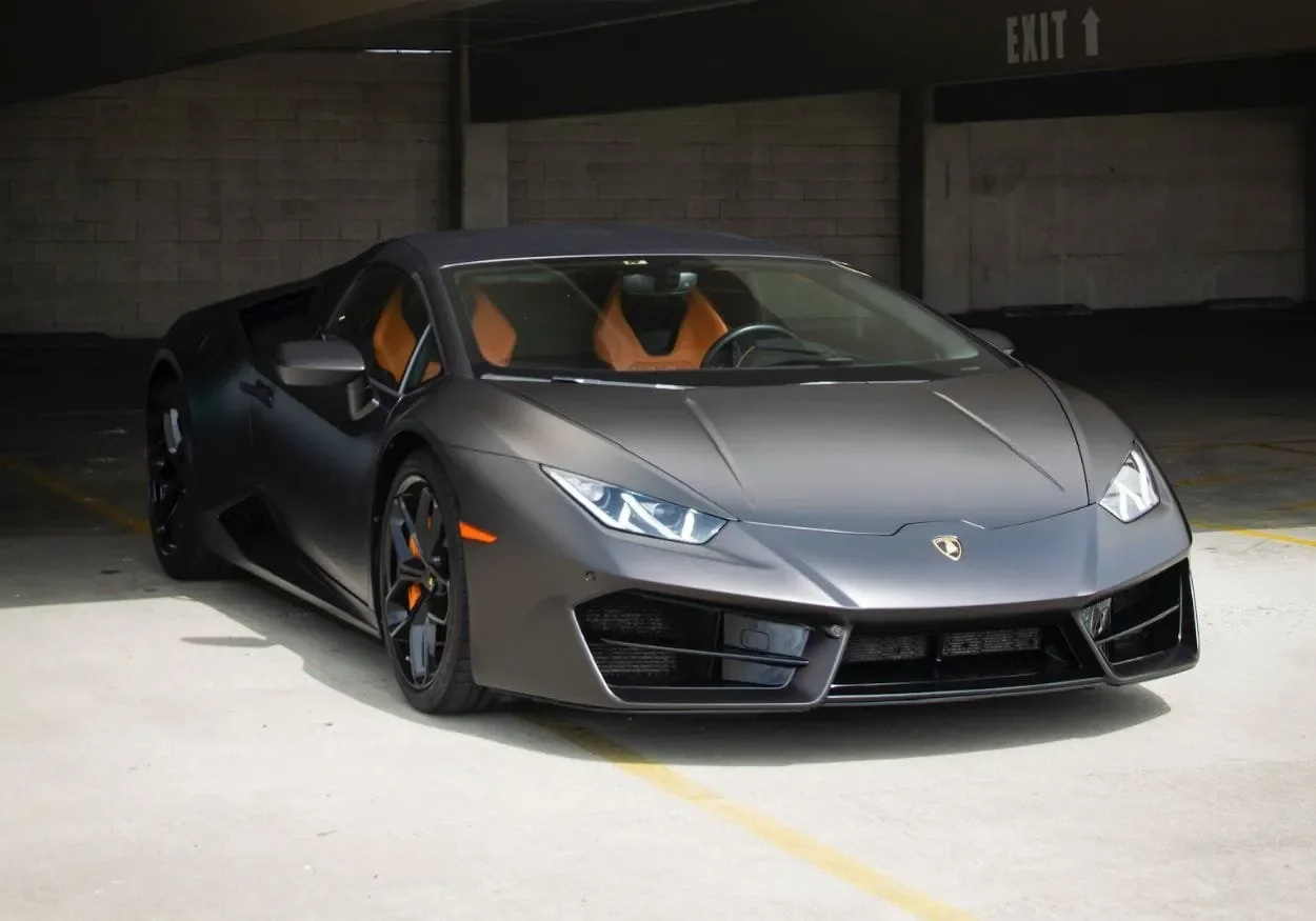 Gray Lamborghini sports car with orange interior seats parked in an underground parking garage.