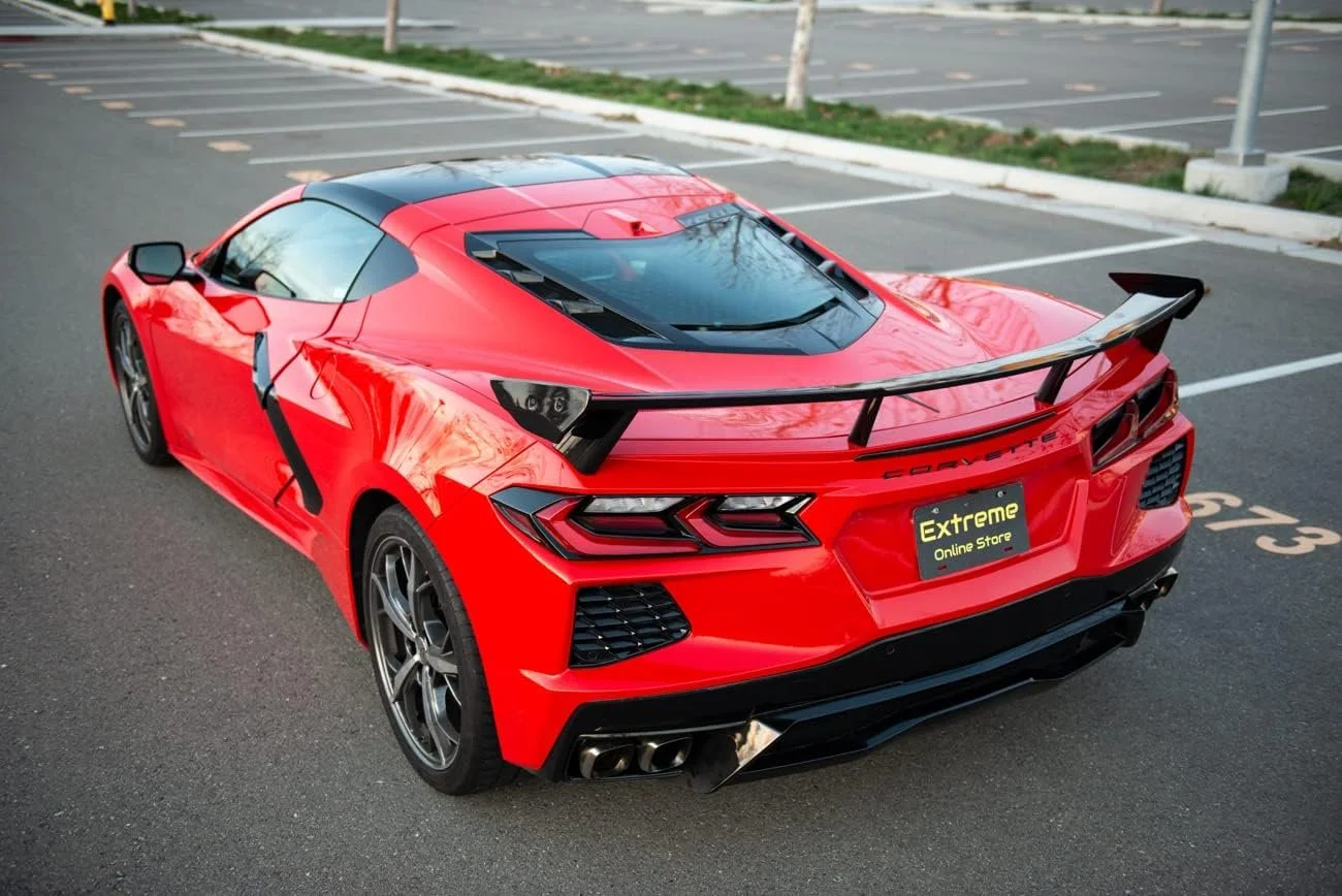 Red Chevrolet Corvette sports car with a large rear spoiler parked in an outdoor parking lot.