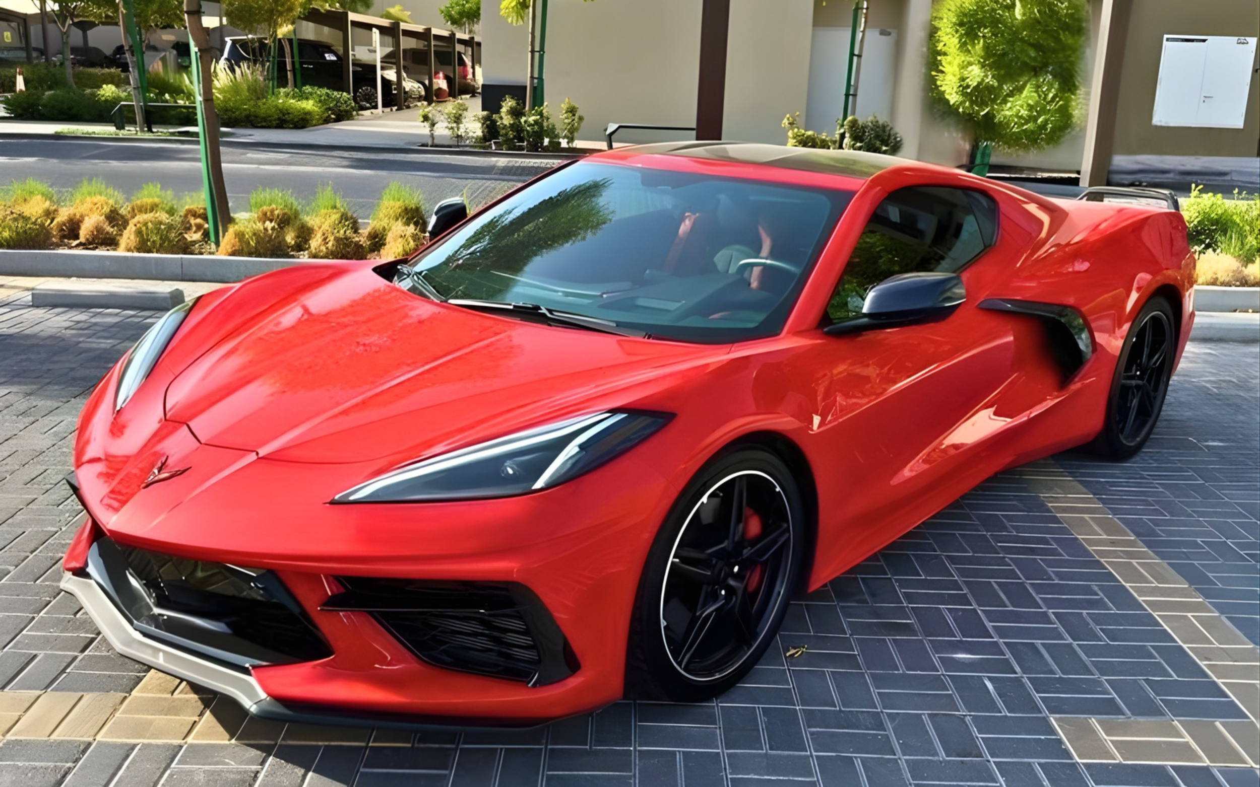 Red sports car parked on a paved area with greenery in the background.