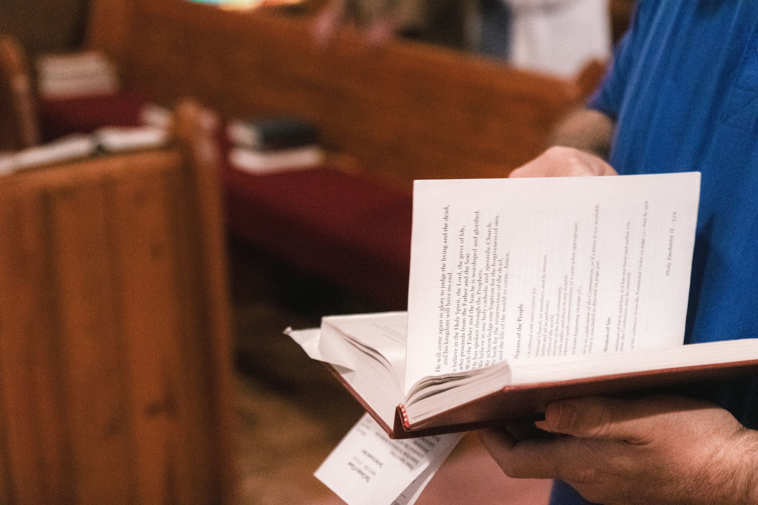 A person holding an open religious book with text emphasized on prayer, standing in a church or similar setting.