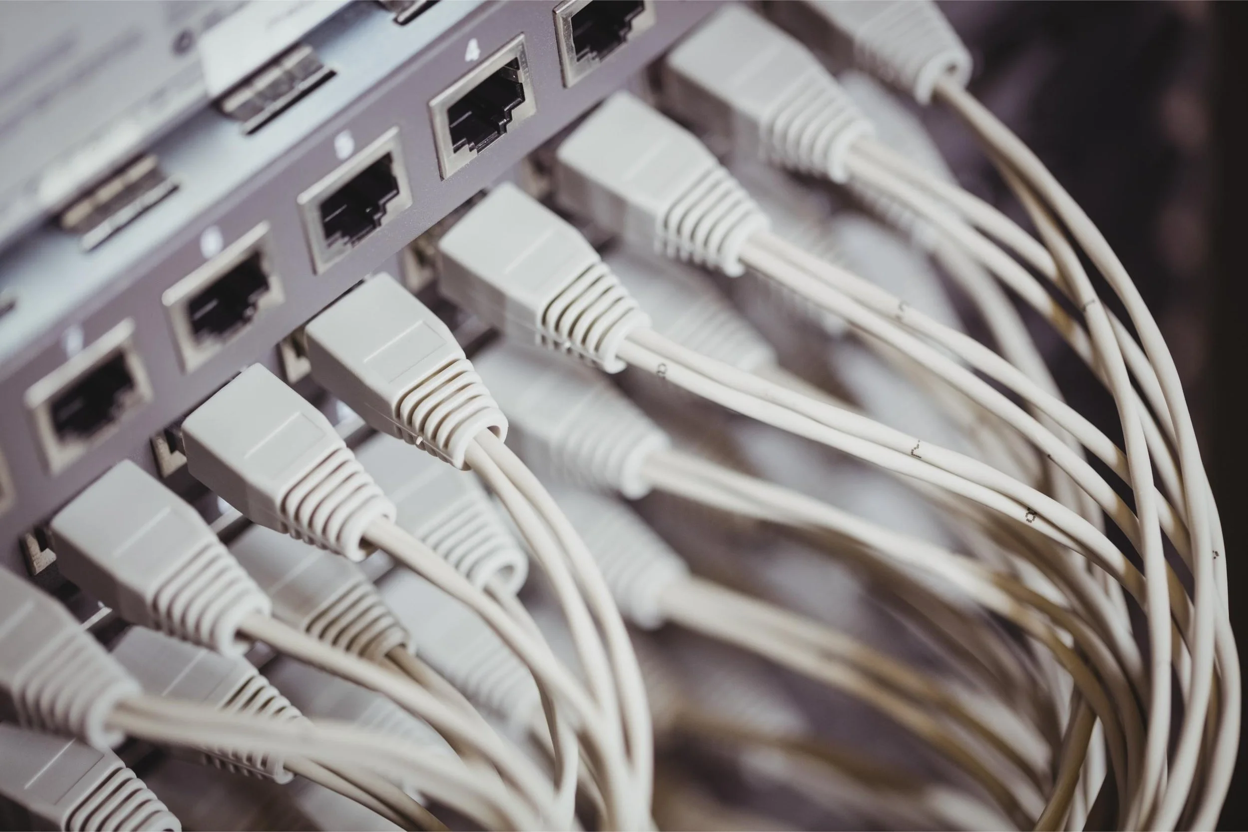 Close-up of a network switch with multiple white Ethernet cables plugged into it.