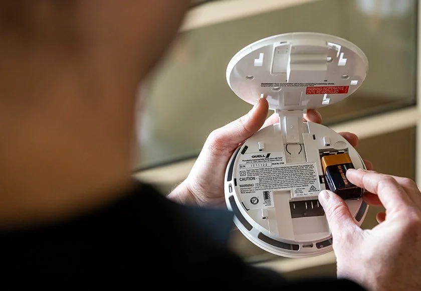 Person replacing the battery in a smoke detector with the cover open.