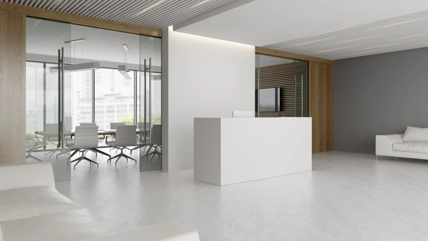 Modern office reception area with white walls, gray accent wall, white sofas, reception desk, and glass-walled conference room with white chairs.