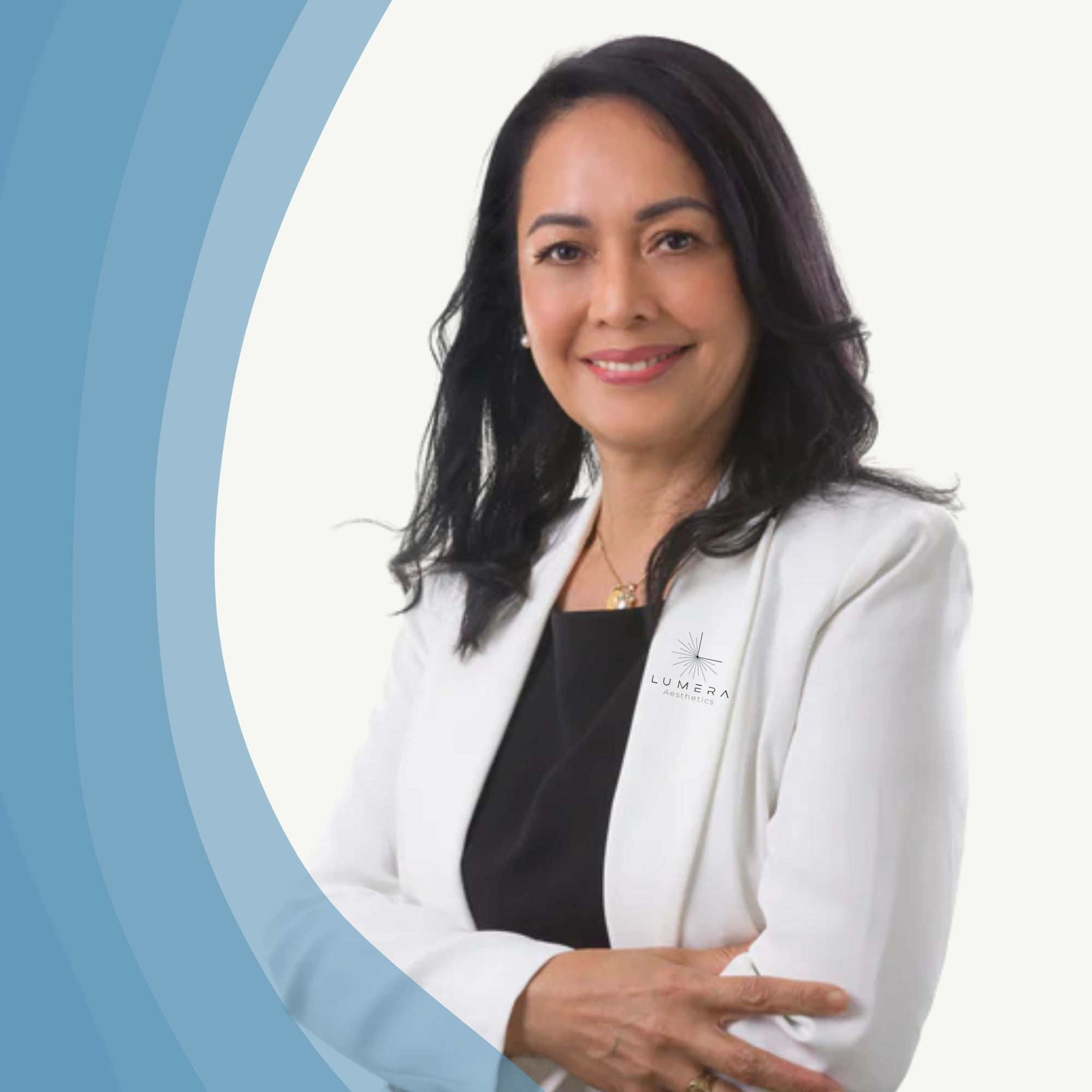 Professional woman with shoulder-length black hair smiling, wearing a white blazer, black top, gold necklace, and a badge with the Lumera Aesthetics logo, standing against a light background with a blue gradient design.