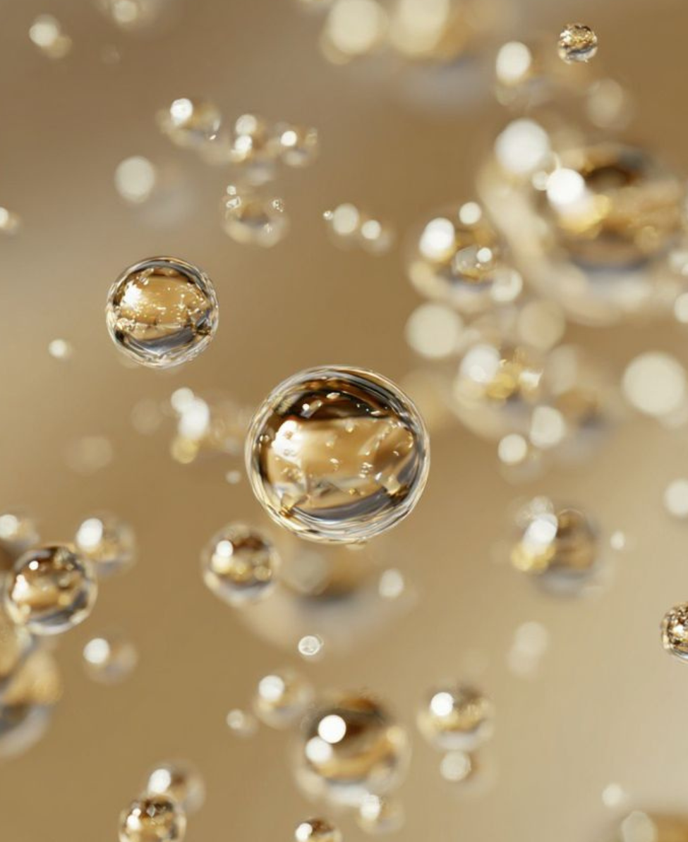 Close-up of bubbles floating in a liquid, with a golden background and reflections within the bubbles.