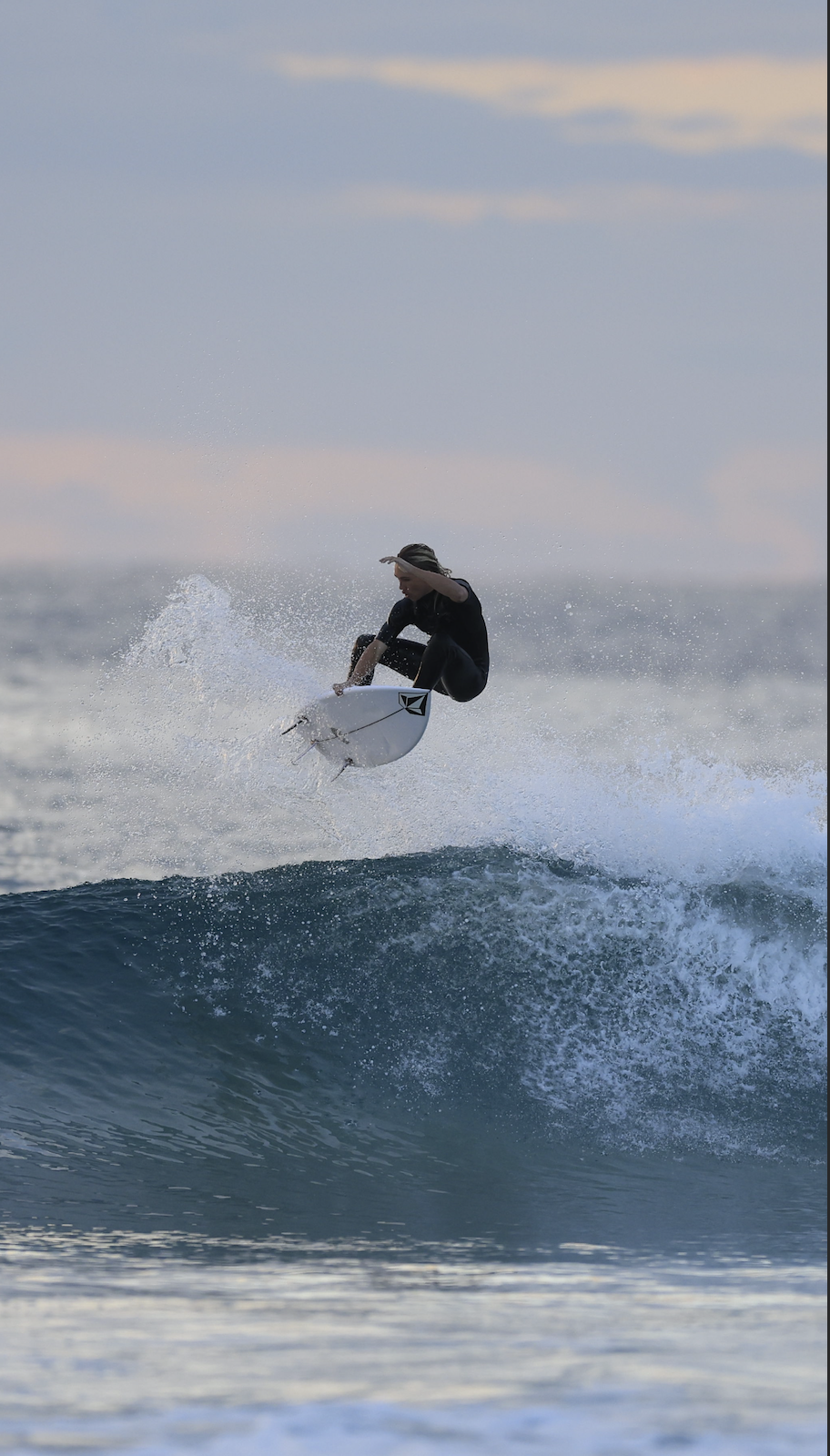 A surfer catching air while riding a wave in the ocean during sunset.