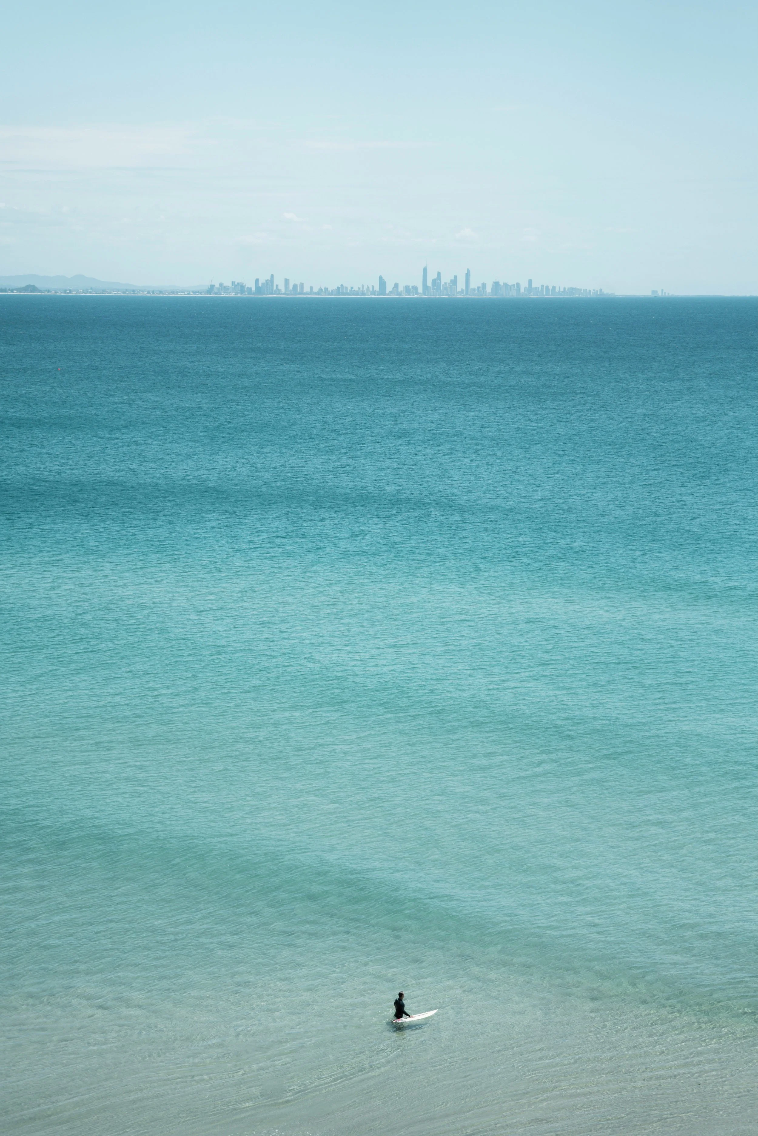 A person paddleboarding on calm ocean waters with a city skyline in the background.