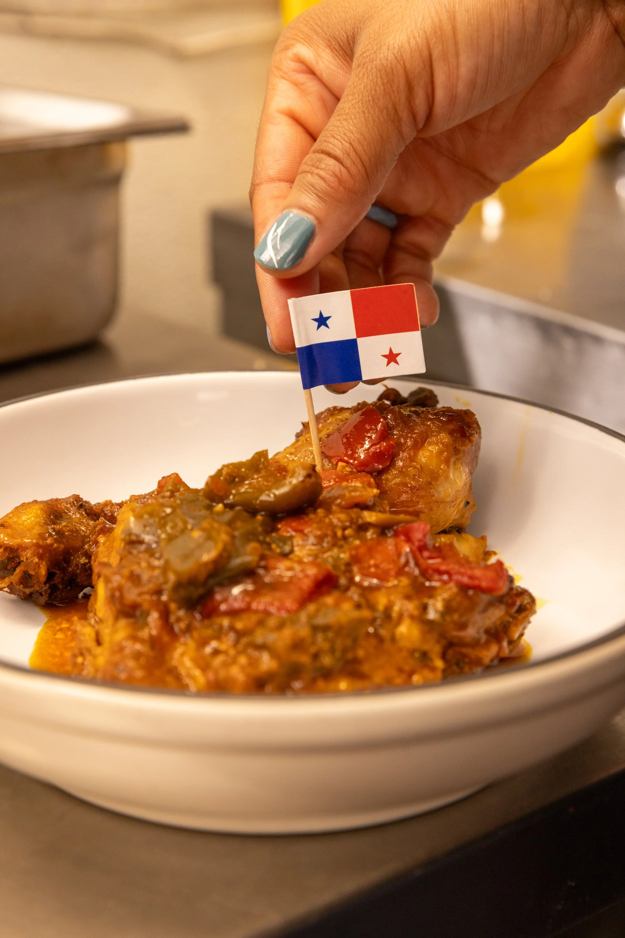 Stew chicken dish in a white bowl, topped with a small Panamanian flag