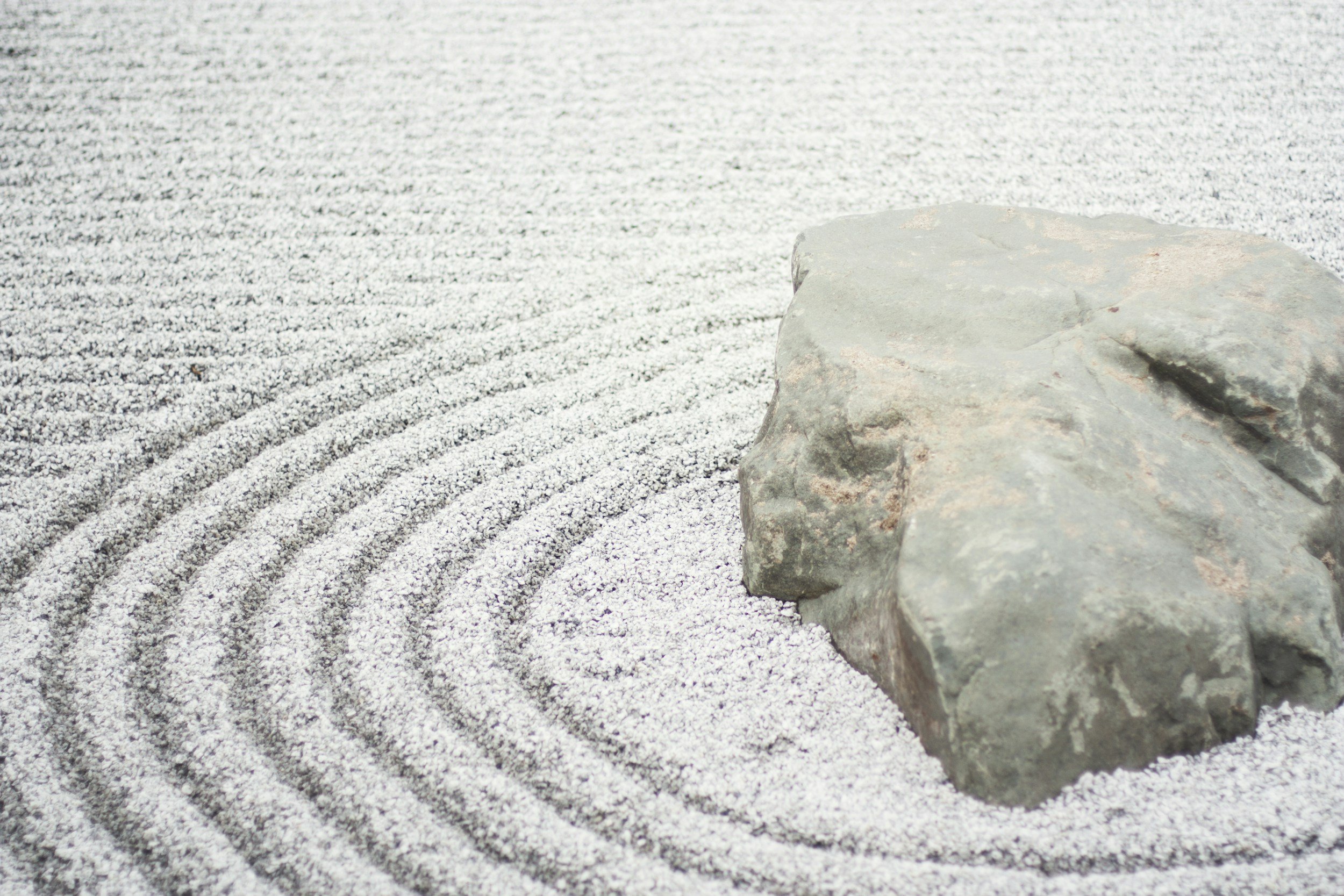 A rock placed in a Zen garden with raked white gravel creating concentric circles around it.