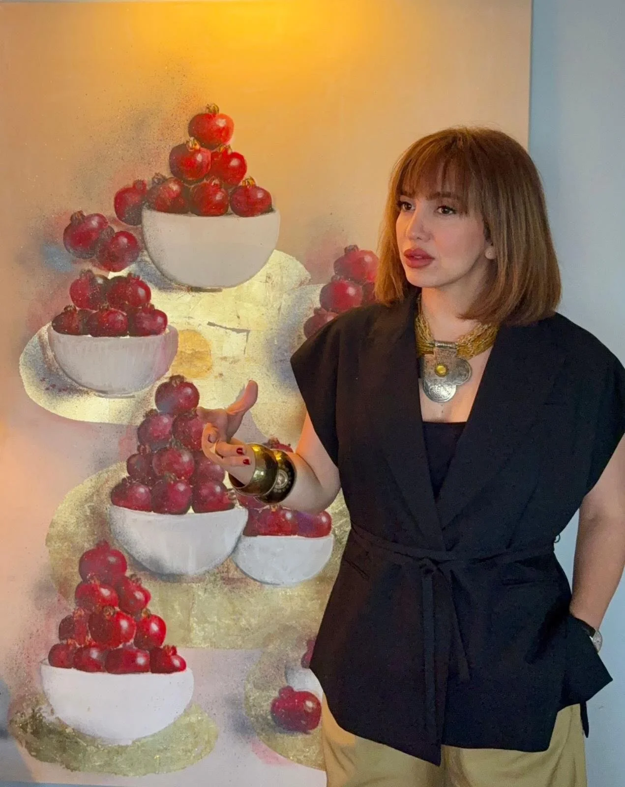 Artist Shade Majlessi standing beside a colorful abstract painting of bowls filled with cherries.