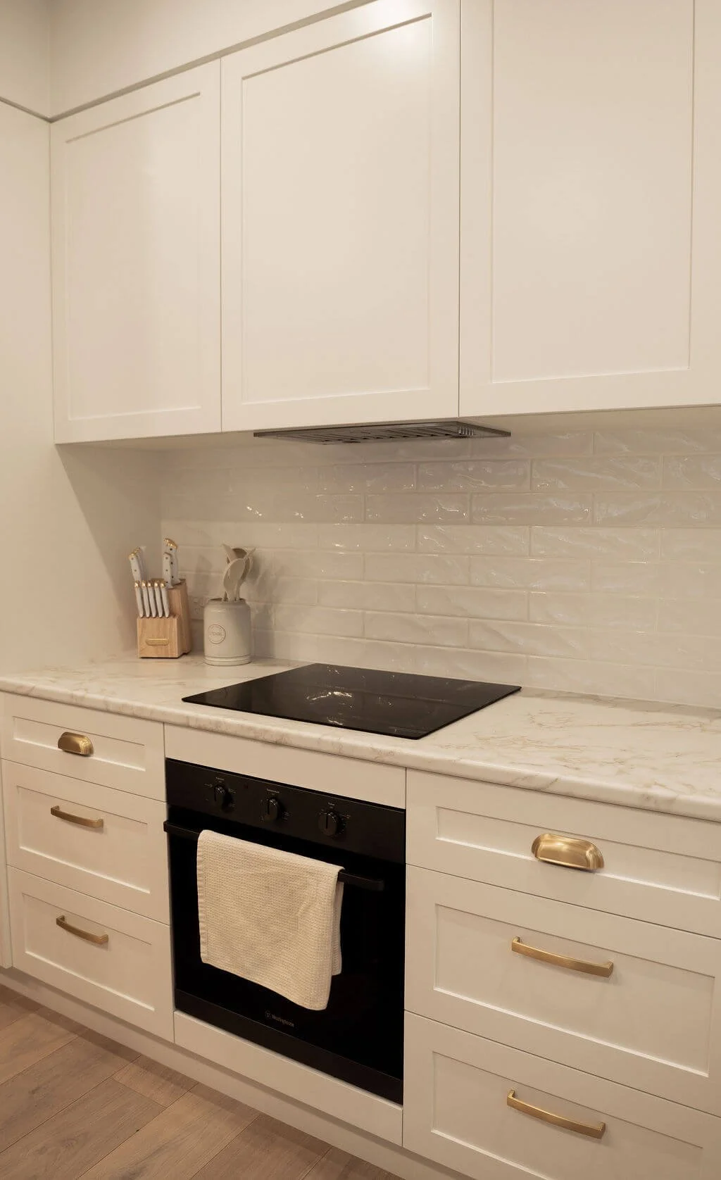 A modern kitchen with white cabinets, a black stove with a beige towel hanging, a marble countertop, and minimal decor.