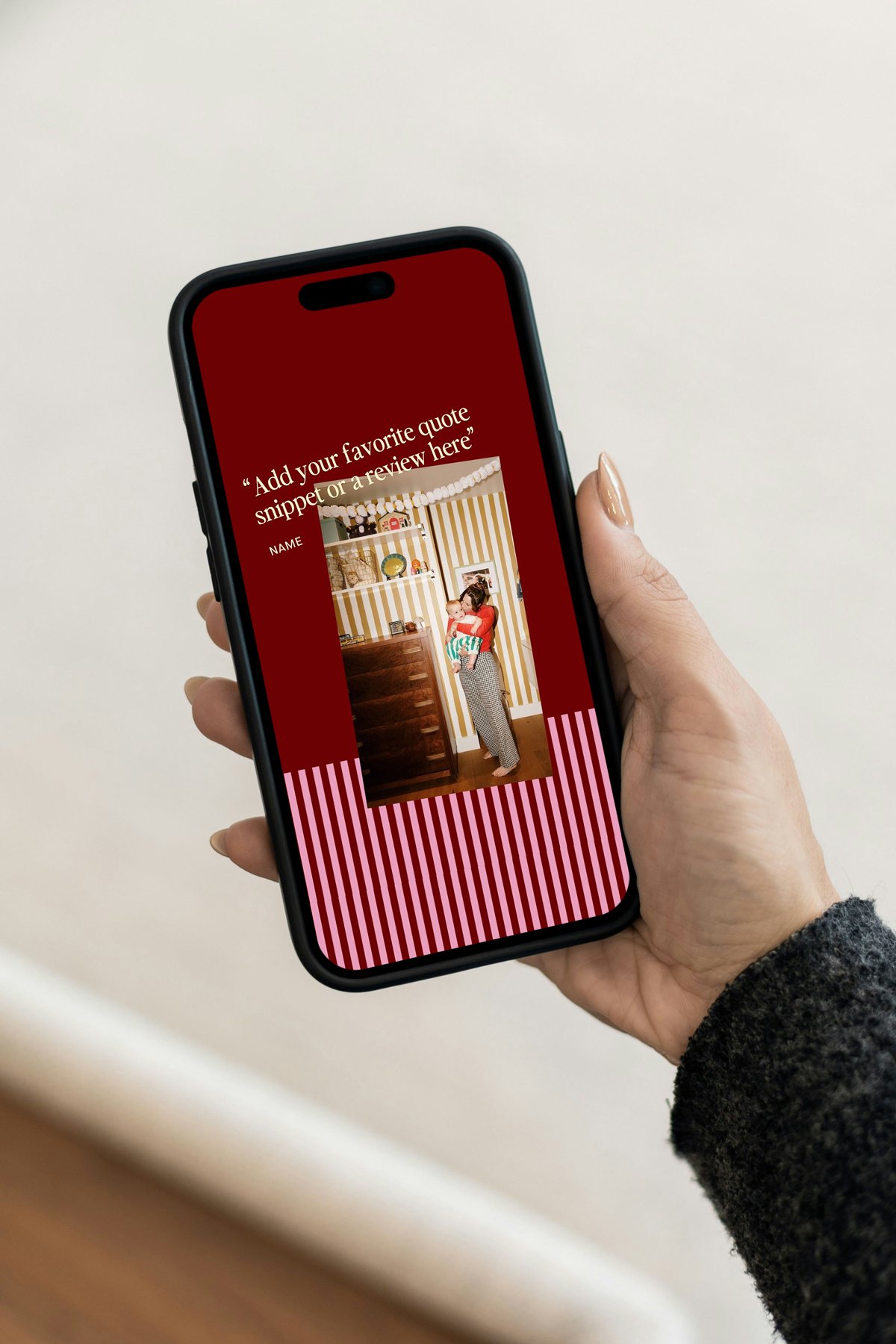 A person holding a smartphone with a photo of a woman holding a child on the screen, with a red background and striped pink and red design at the bottom. 
